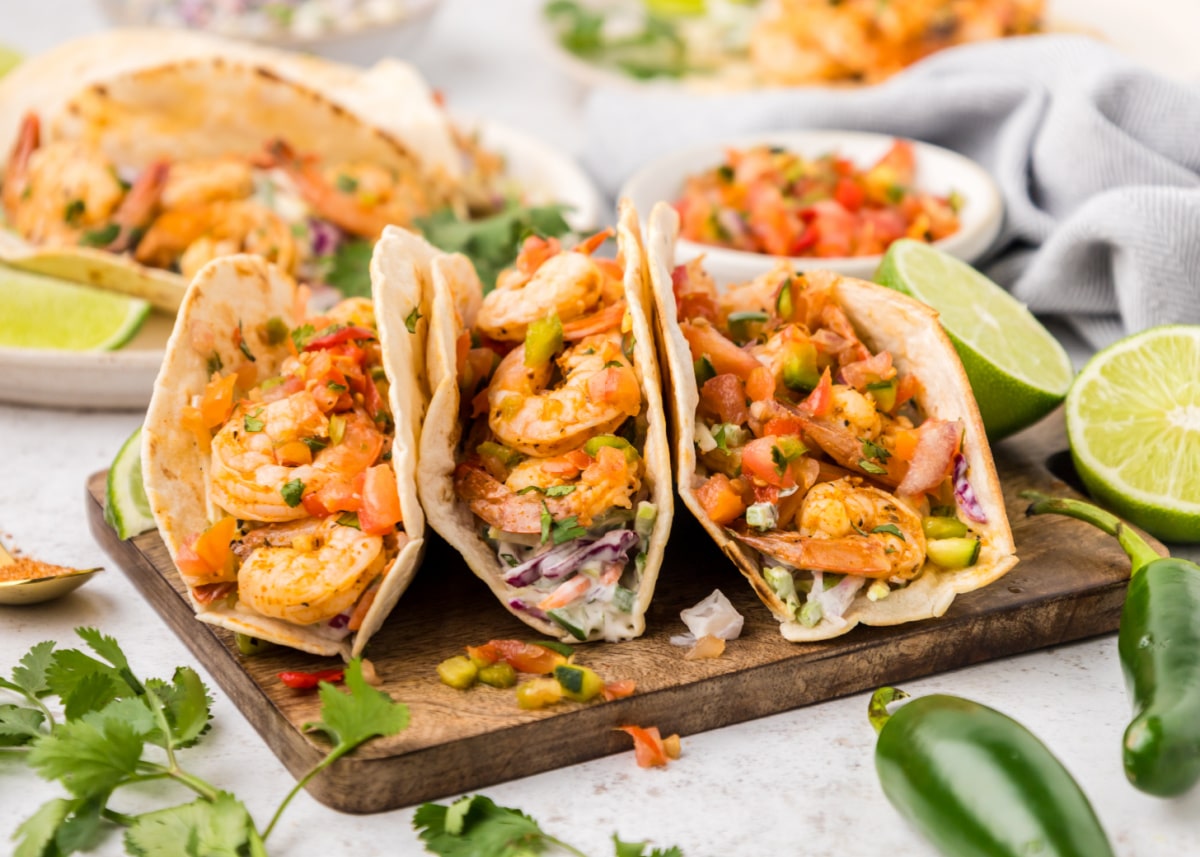 three Cajun Shrimp Tacos Three Cajun shrimp tacos surrounded by fresh ingredients like cilantro, lime, and jalapeños