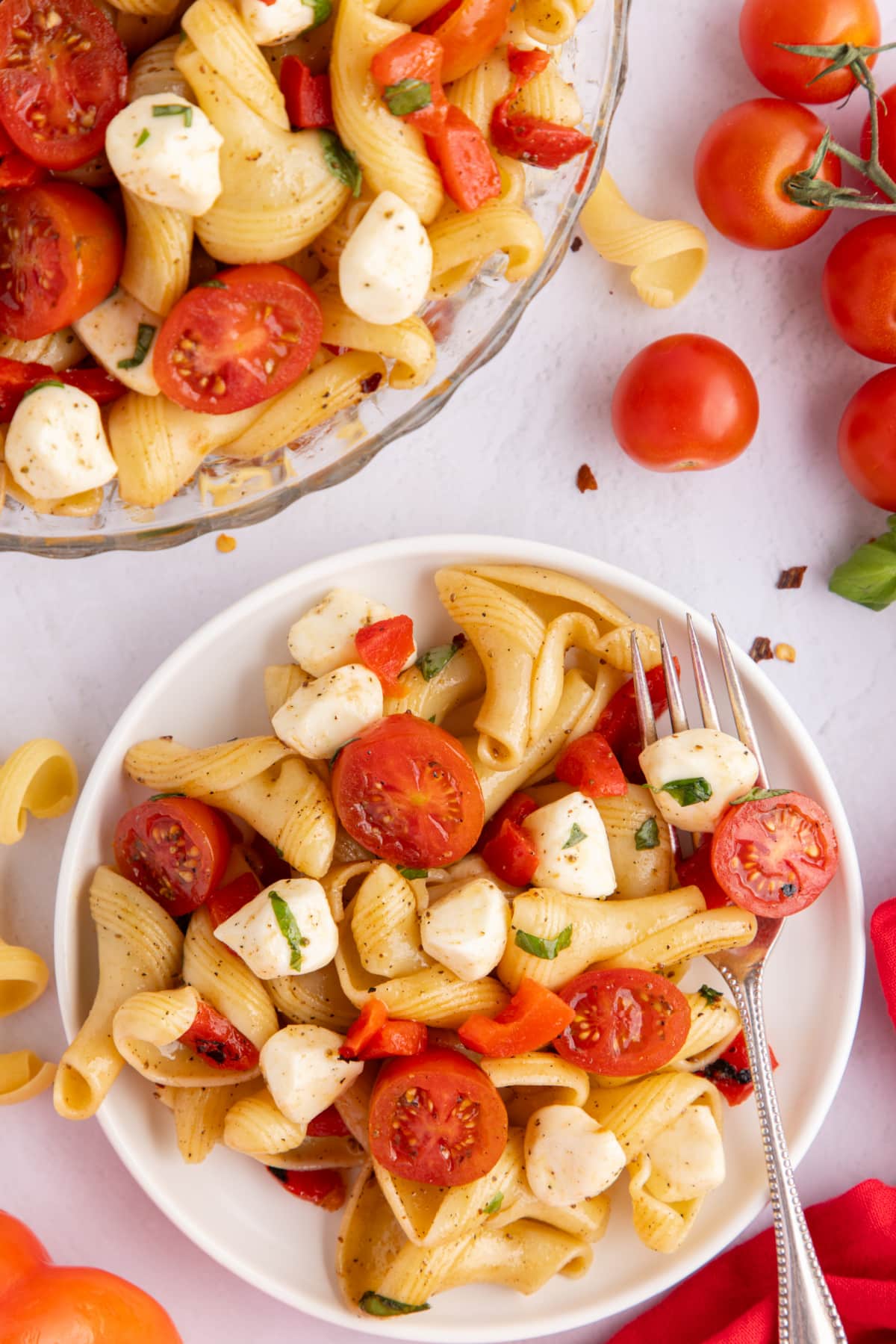 Caprese Pasta Salad with Roasted Red Peppers on a plate Single serving of caprese pasta salad on a white plate with a fork beside it, showing the mix of colorful ingredients.