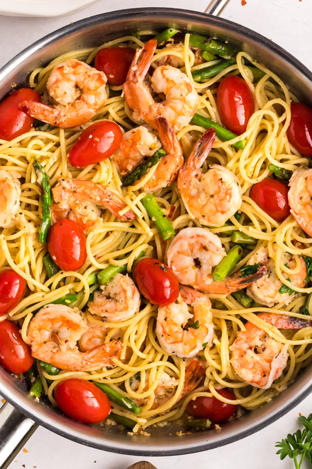 a skillet of Garlic Shrimp Pasta with Asparagus and Tomatoes Close-up overhead shot of garlic shrimp pasta in a skillet, showing shrimp, asparagus, and tomatoes mixed with spaghetti.