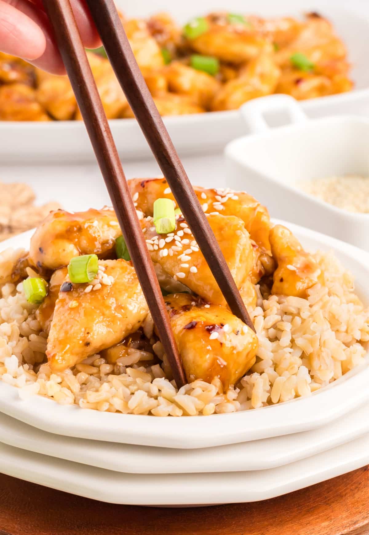 Honey Sesame Chicken with chopsticks Close-up of honey sesame chicken over rice, with chopsticks lifting a bite.