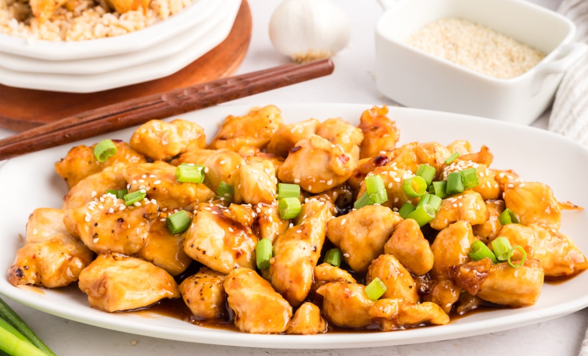 Honey Sesame Chicken on a platter Side view of a serving platter filled with honey sesame chicken, topped with sesame seeds and green onions.