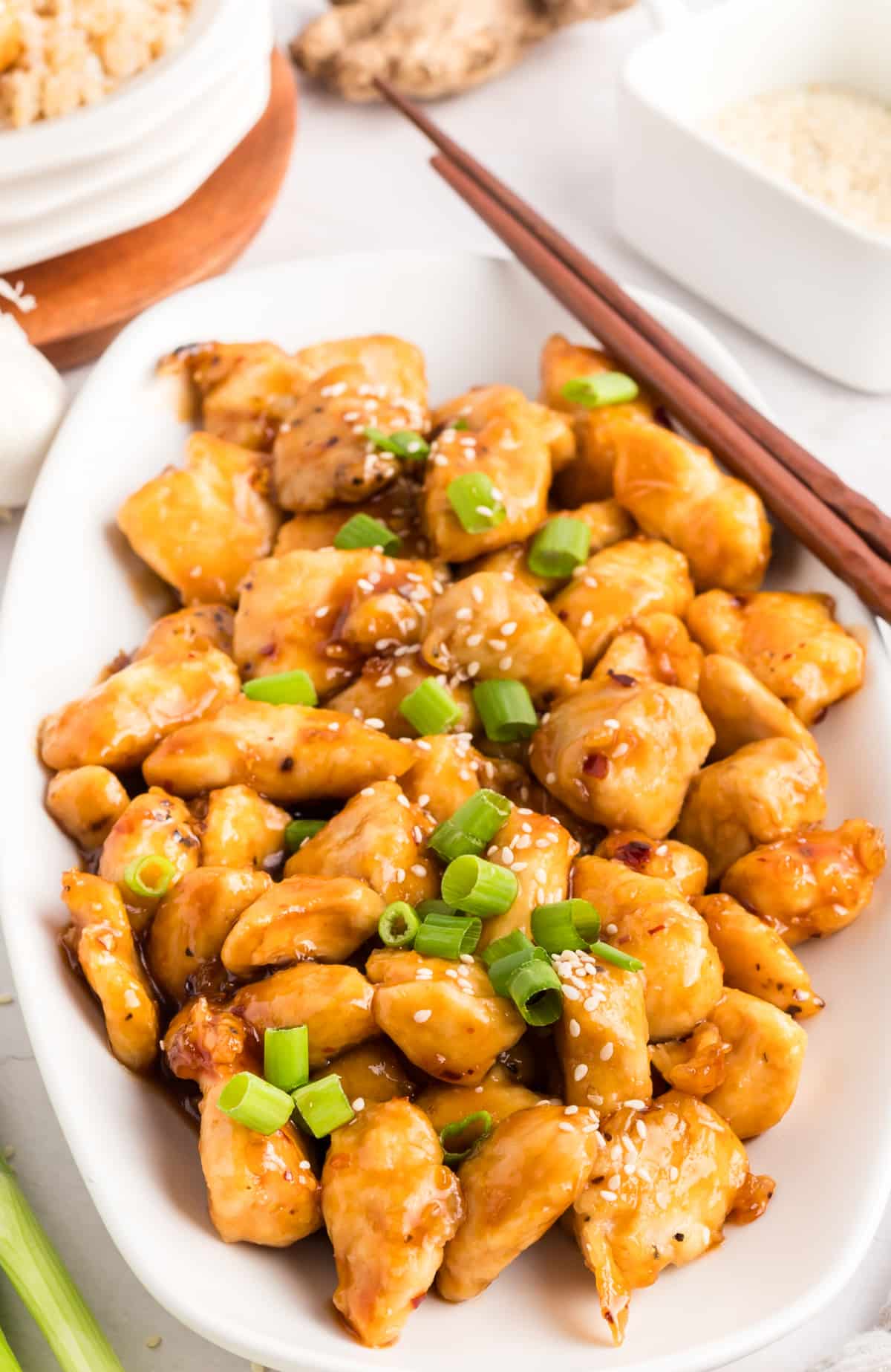 Honey Sesame Chicken ready to serve Top-down view of honey sesame chicken on a white platter, garnished with sliced green onions.