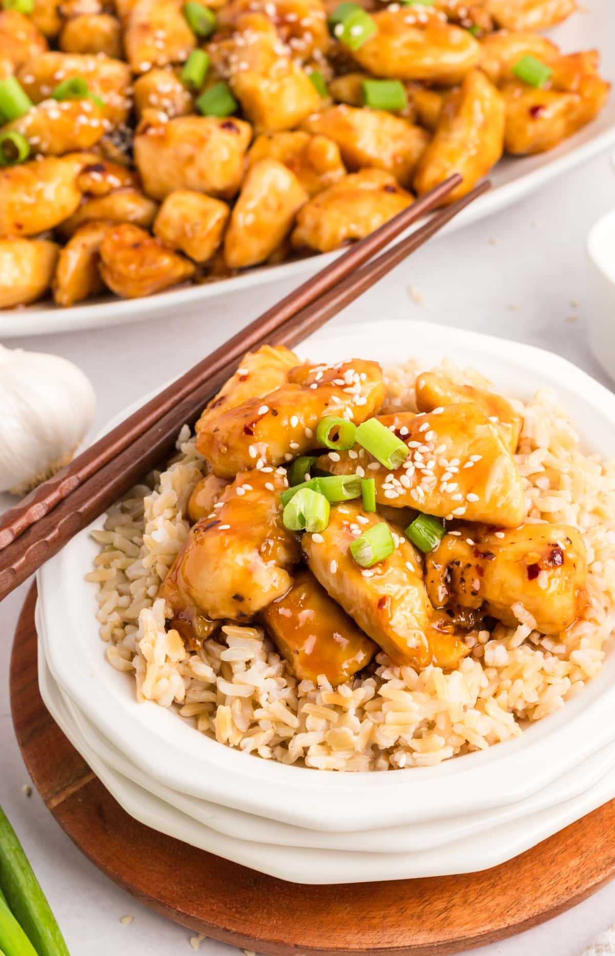 Honey Sesame Chicken on a bed of rice Honey sesame chicken served over white rice on a white plate, with chopsticks resting beside the dish.