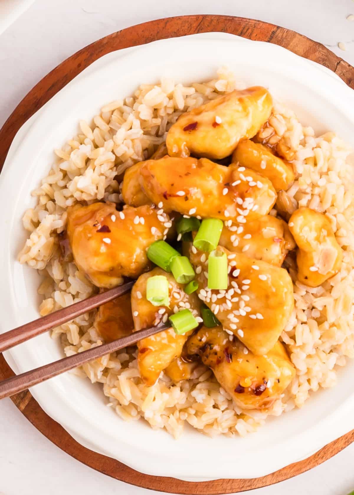 better than takeout Honey Sesame Chicken Overhead shot of a single serving of honey sesame chicken on a plate, with sauce and garnishes visible.