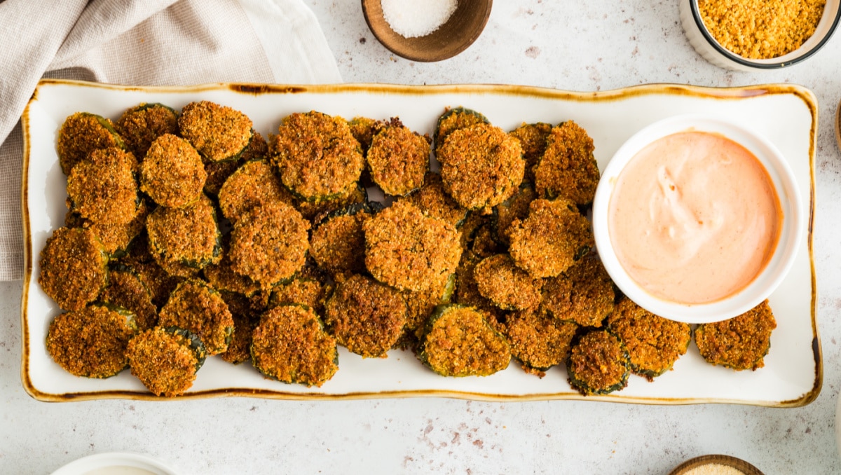 Overhead view of a serving platter of oven fried dill pickles with a small bowl of dipping sauce.