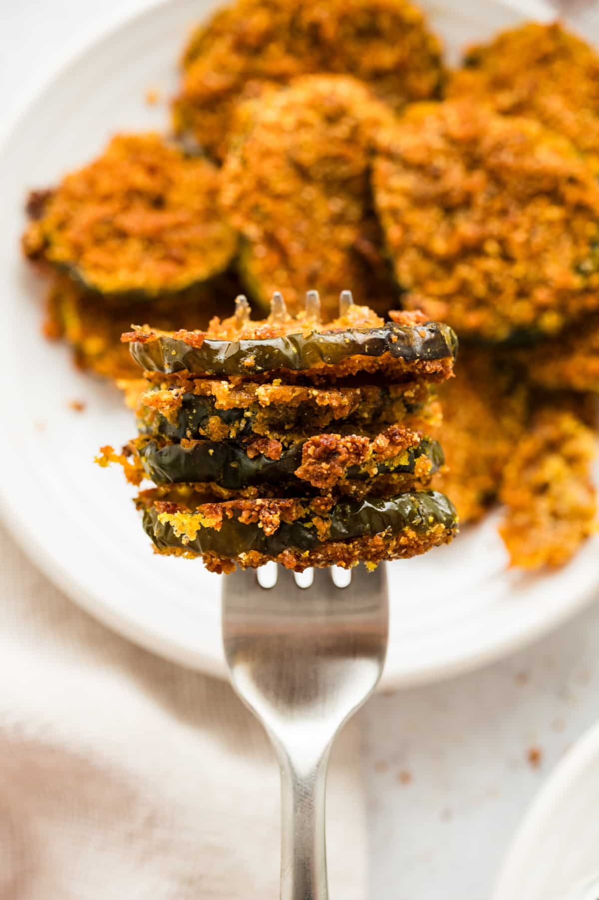 Fork holding several oven fried dill pickles with more pickles scattered in the background.
