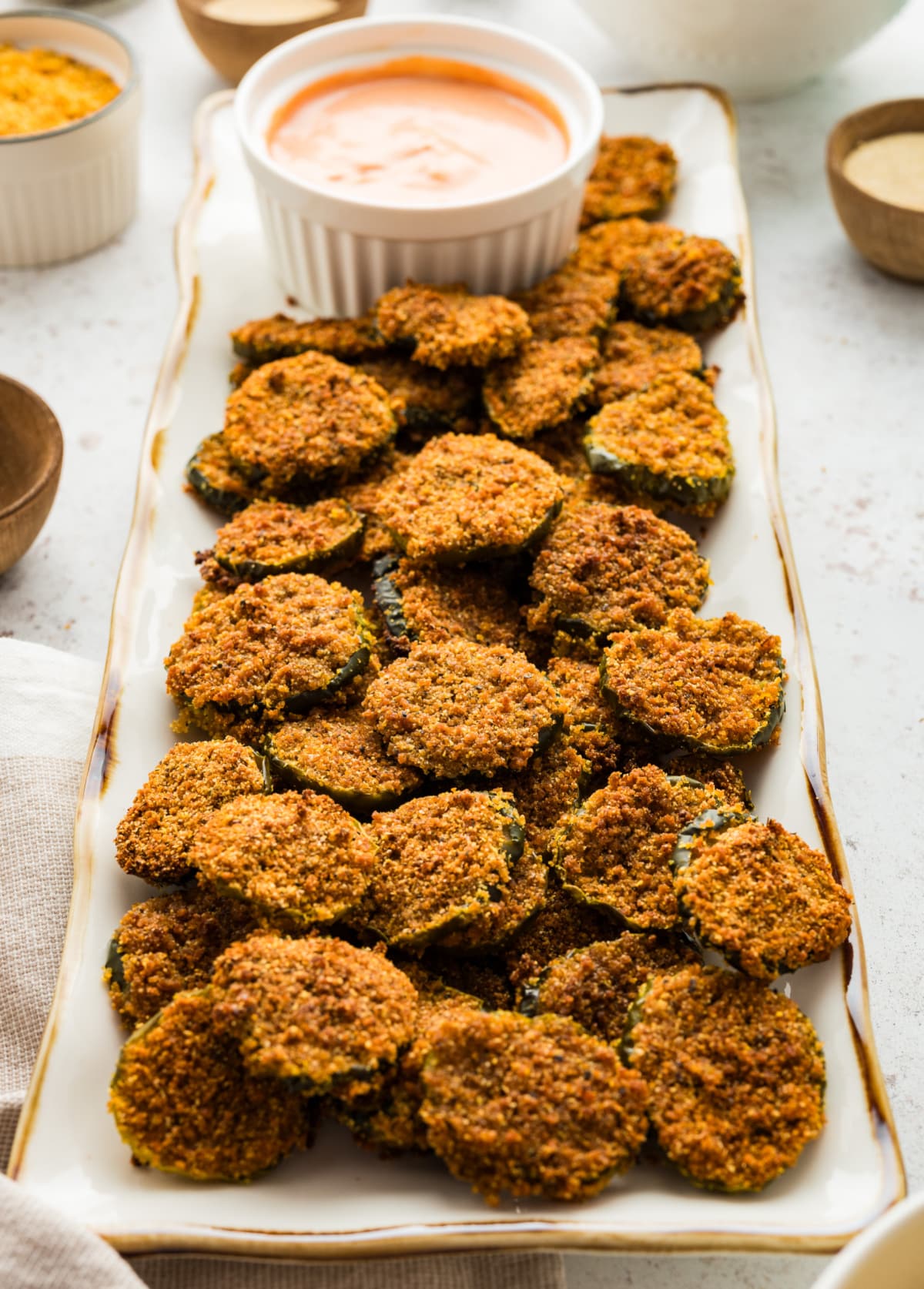 Side view of a platter of oven fried dill pickles served with dipping sauce.