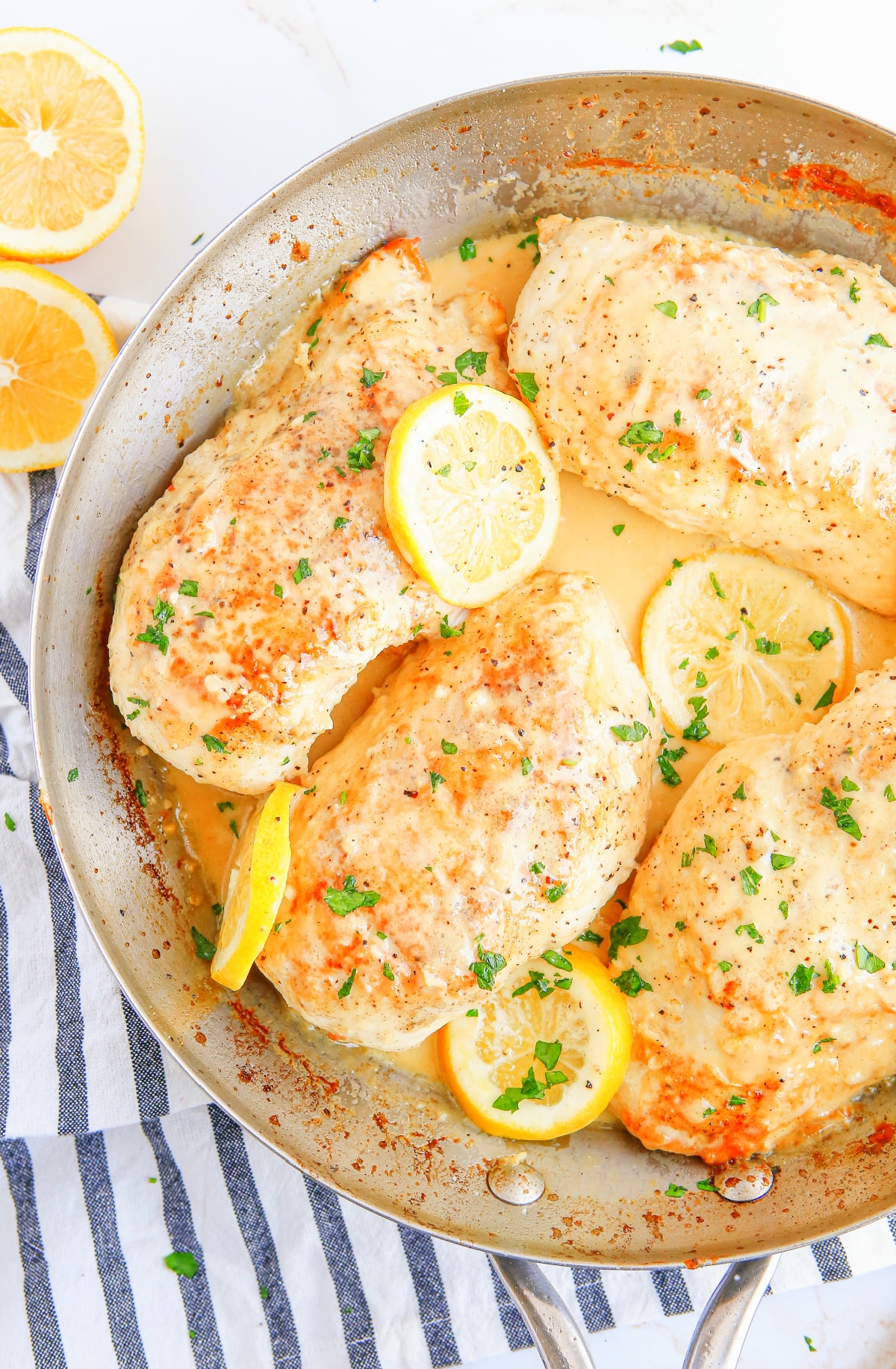 top-down view of skillet creamy lemon garlic chicken garnished with parsley and lemon slices. 