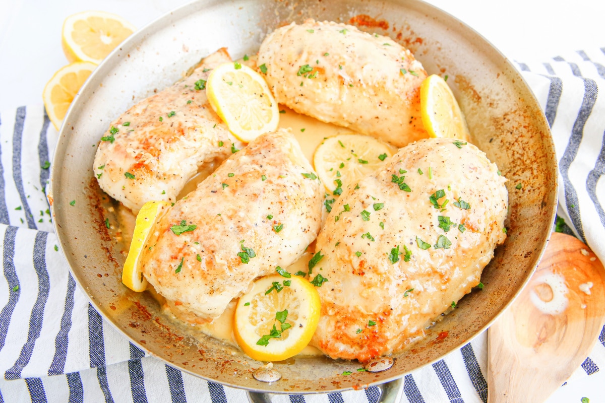 Side-angle shot of golden brown chicken breasts simmering in a creamy lemon garlic sauce.