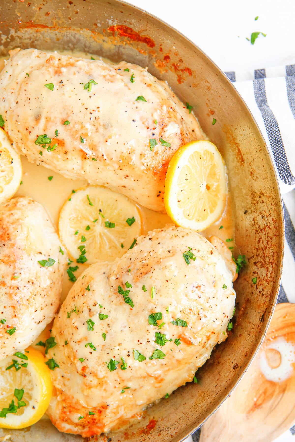 Close-up overhead image of half the skillet showing juicy chicken breasts in a creamy garlic sauce with lemon slices.