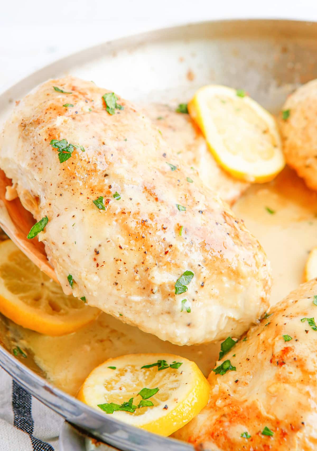 Wooden spoon lifting a saucy piece of chicken breast out of the skillet, showing texture and thickness of the sauce.