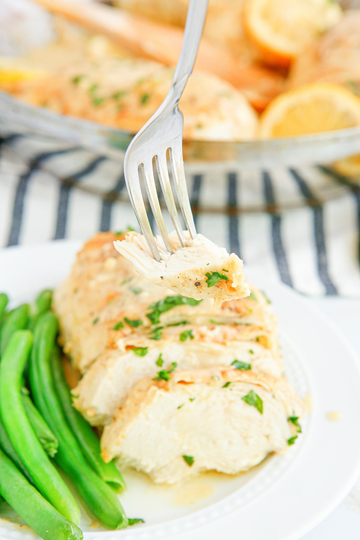 Plate of sliced creamy lemon garlic chicken served with green beans, with a fork holding up a bite-sized piece.
