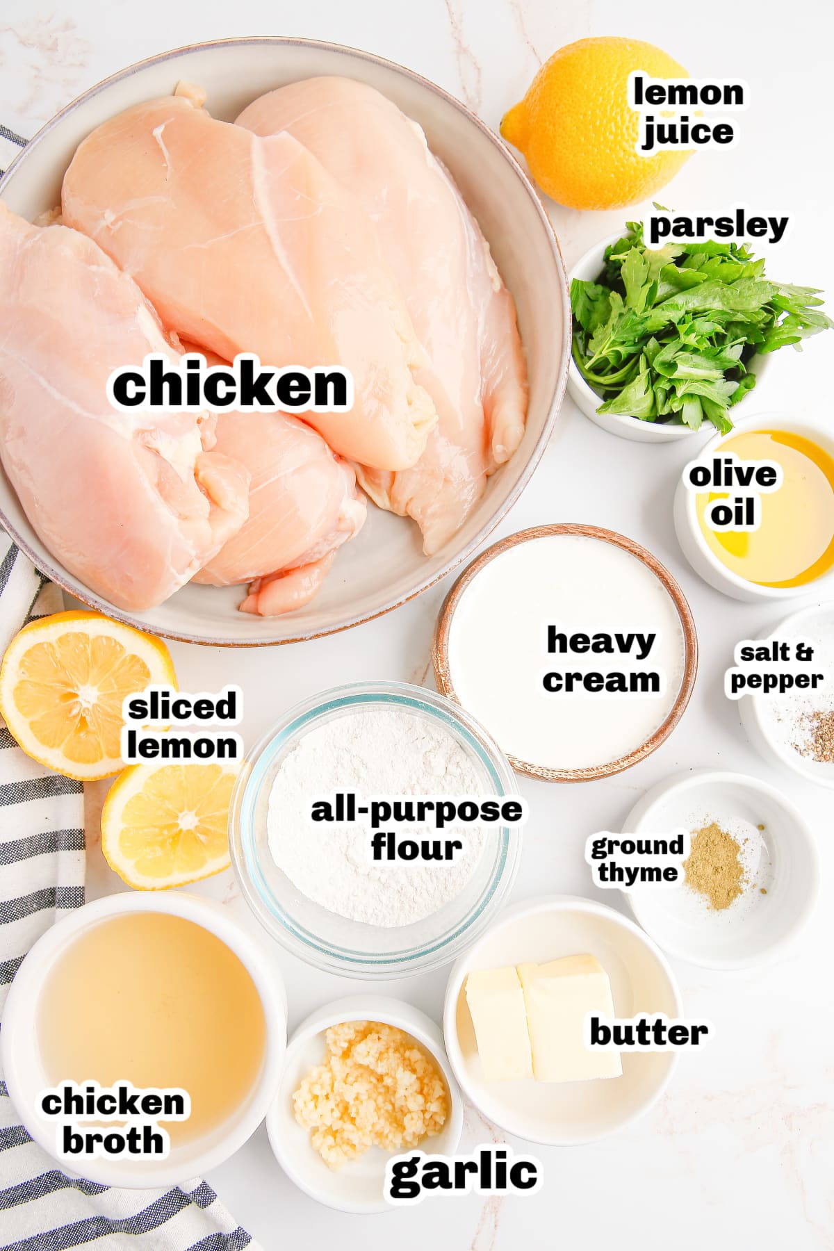 Overhead shot of ingredients laid out for skillet creamy lemon garlic chicken, including chicken breasts, lemon, garlic, and cream.