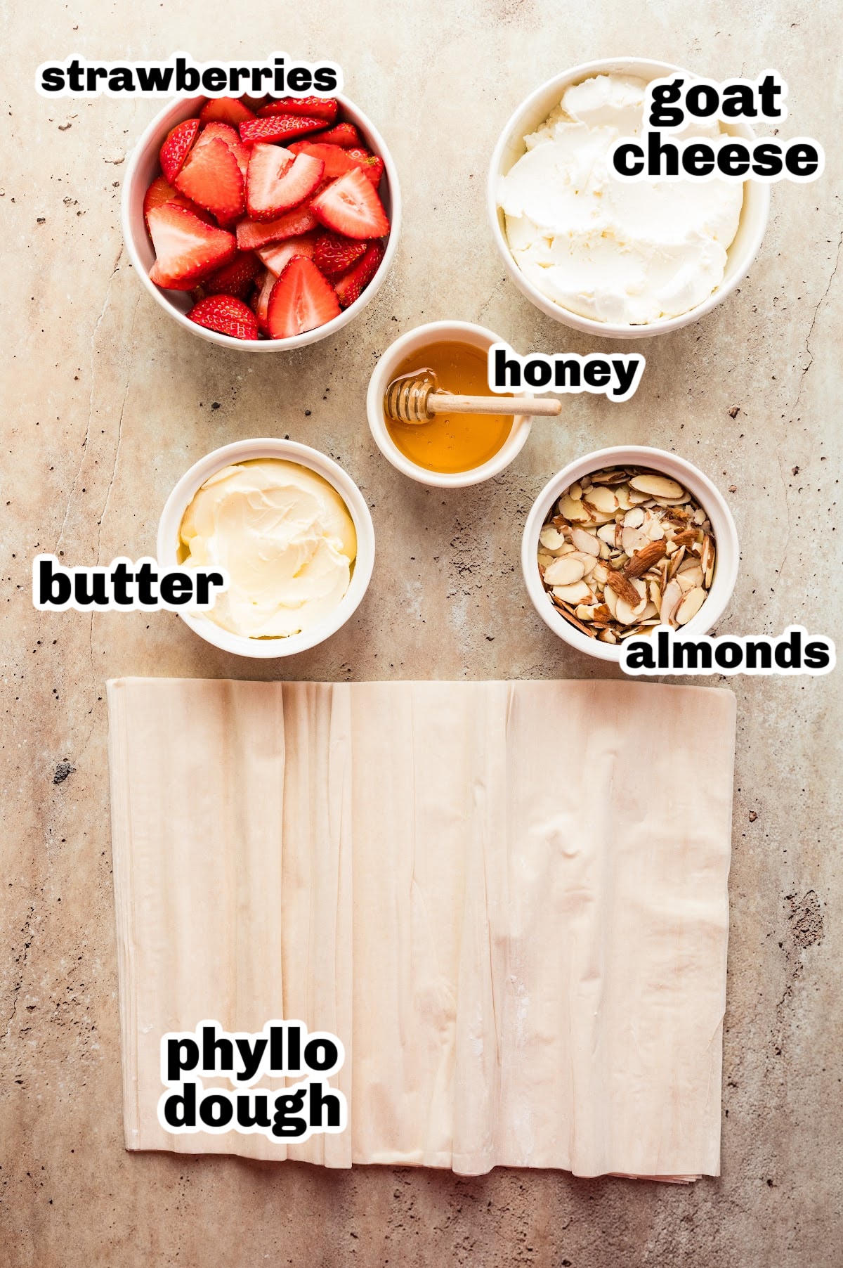 All ingredients laid out for making the strawberry goat cheese tart, including phyllo dough, goat cheese, strawberries, honey, almonds, and butter.