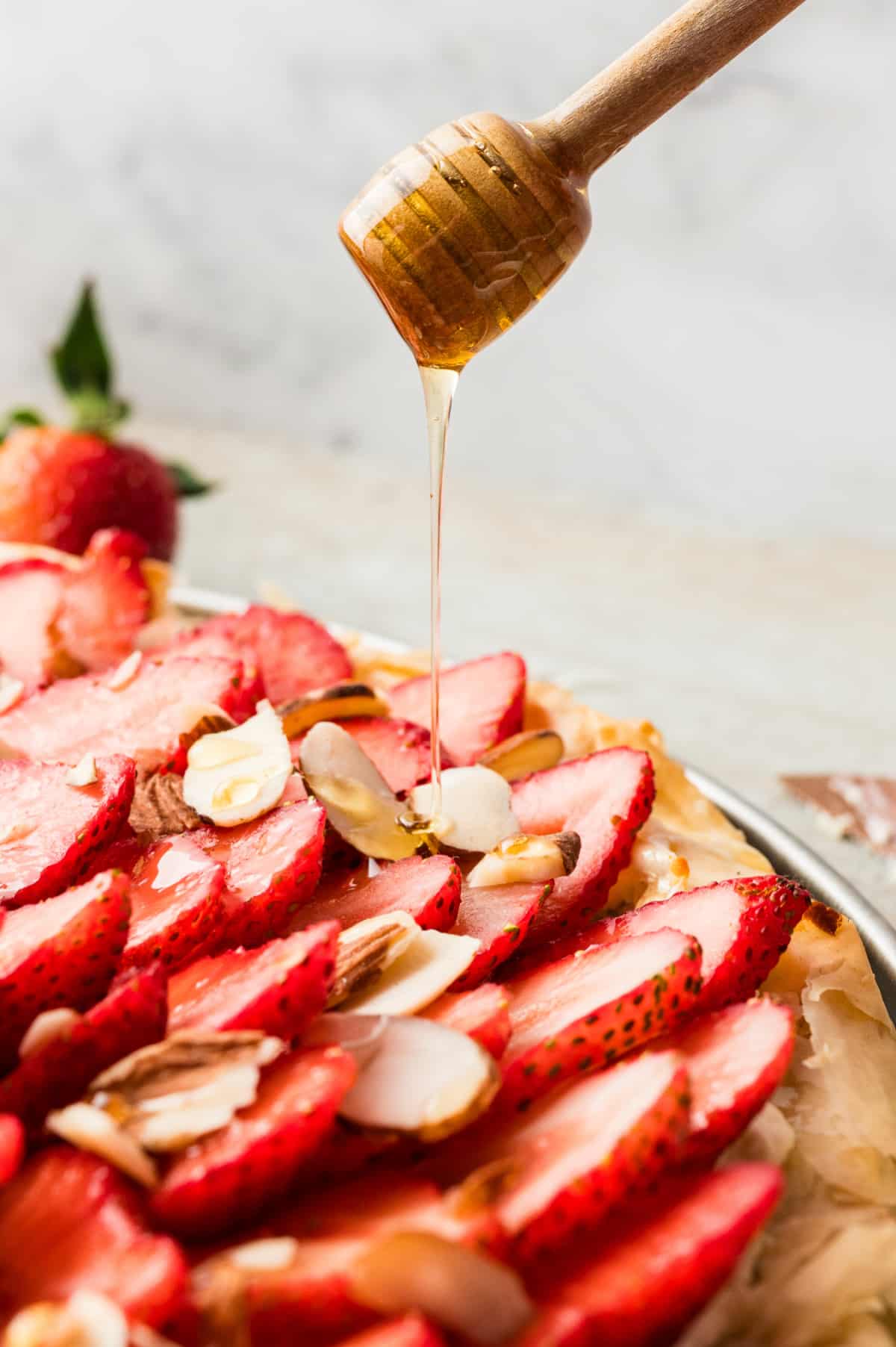 Close-up of a honey wand drizzling honey over a slice of the strawberry goat cheese tart.