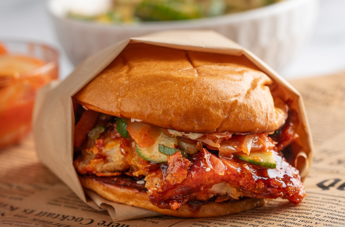 Front view of sandwich with Gochujang sauce and potato chip-crusted chicken Head-on view of the full sandwich showing layers of crispy chicken, sauce, and toppings