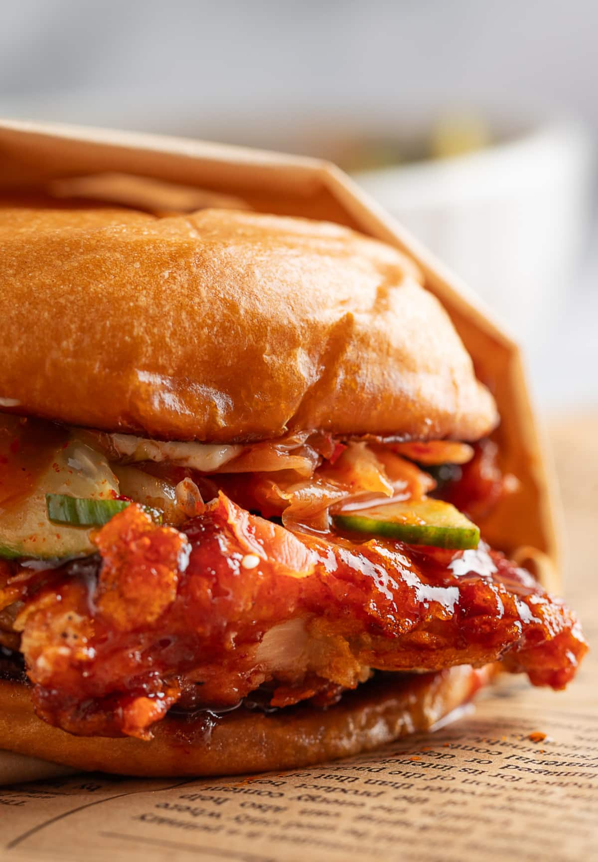 Gochujang Chicken Sandwich stacked high with salad and kimchi Side view of Gochujang Chicken Sandwich showing crispy crust, cucumber salad, and kimchi stacked on a roll