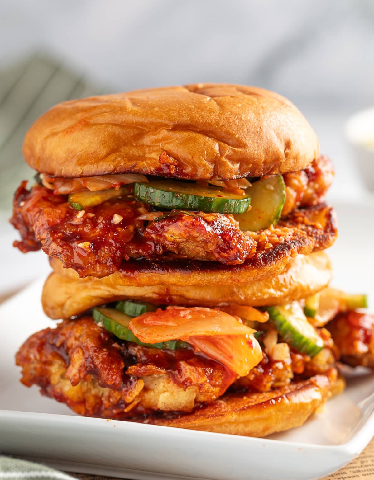 Two stacked Gochujang Chicken Sandwiches with potato chip crust and Gochujang sauce Front view of two Gochujang Chicken Sandwiches stacked on top of each other with crispy crust and messy toppings