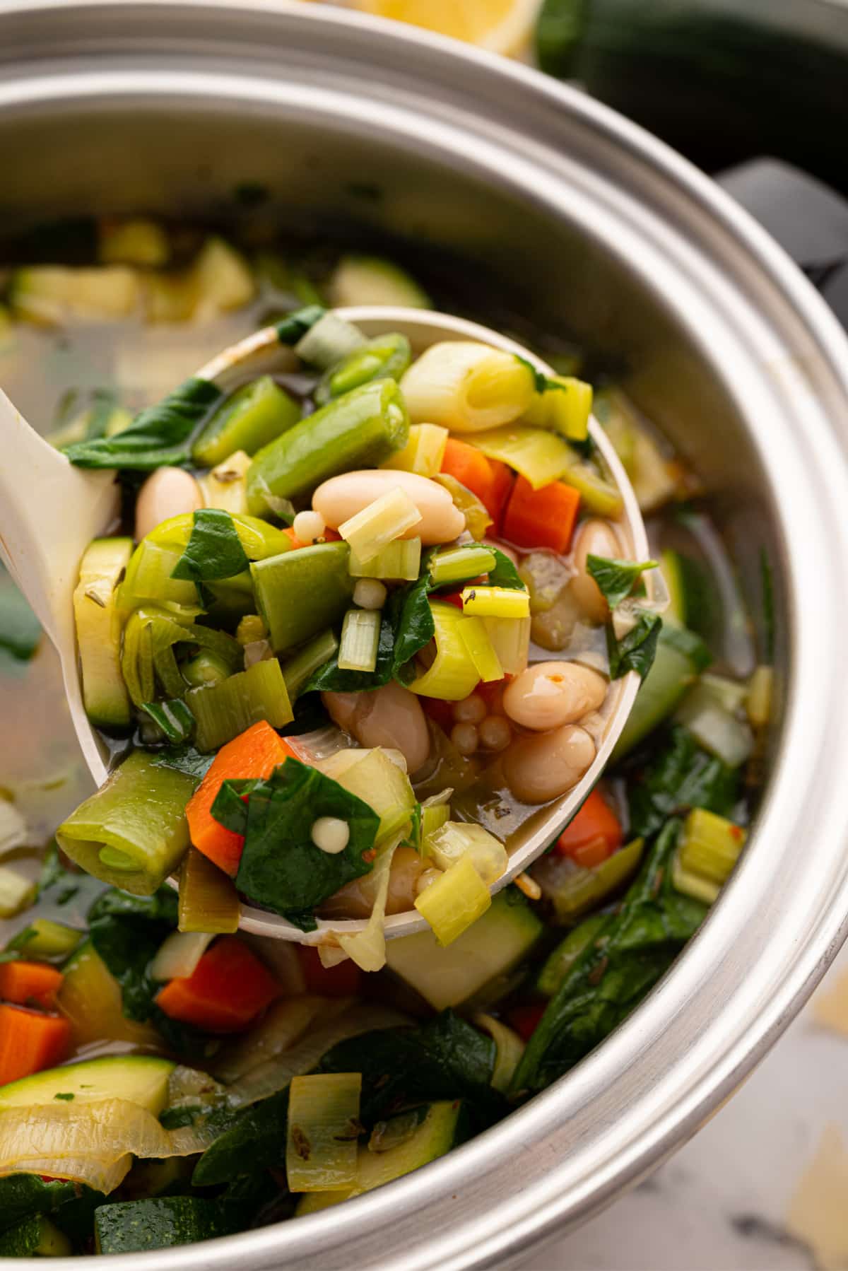 Ladle of green minestrone lifted over the soup pot A full ladle of green minestrone lifted over the pot, showing pasta, beans, and bright vegetables