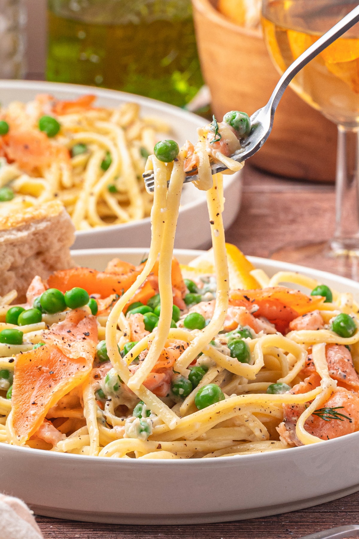 Fork lifting a bite of creamy smoked salmon pasta with lemon and dill. Side view of a fork taking a bite of smoked salmon pasta from a plate.