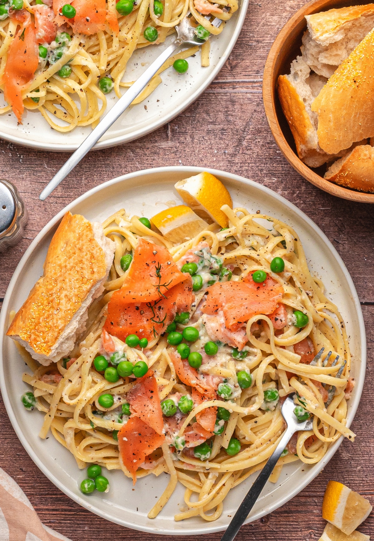 Smoked salmon pasta with lemon, dill, and peas on a plate with bread. Top view of smoked salmon pasta with lemon and dill served with crusty bread.