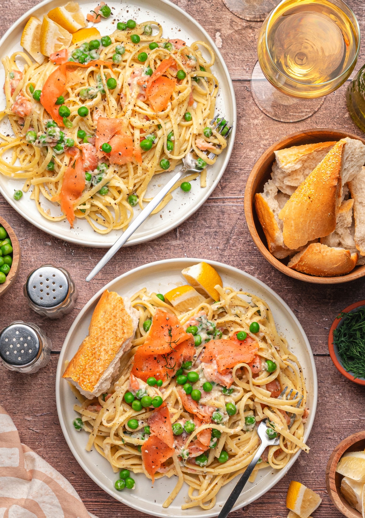 Finished plates of creamy smoked salmon pasta with fresh dill and peas. Top view of two plates of smoked salmon pasta with lemon and dill, ready to eat.