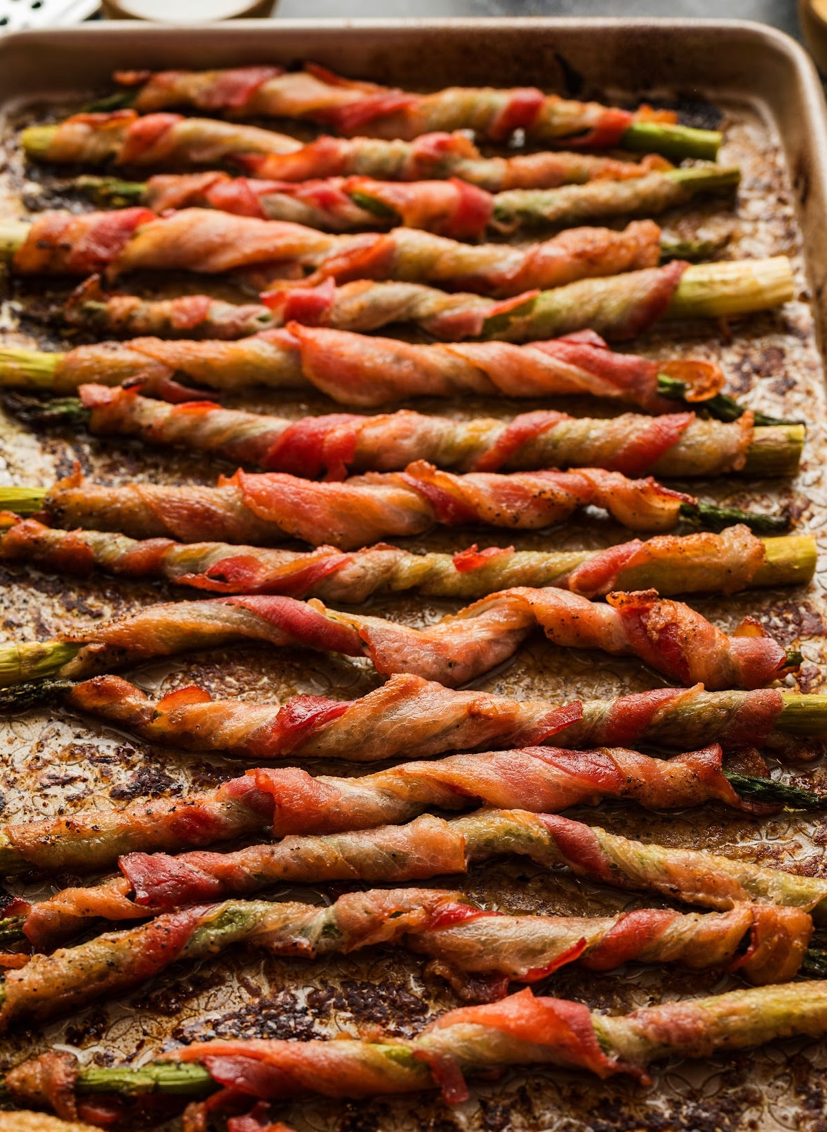 Full baking sheet with rows of roasted bacon-wrapped asparagus