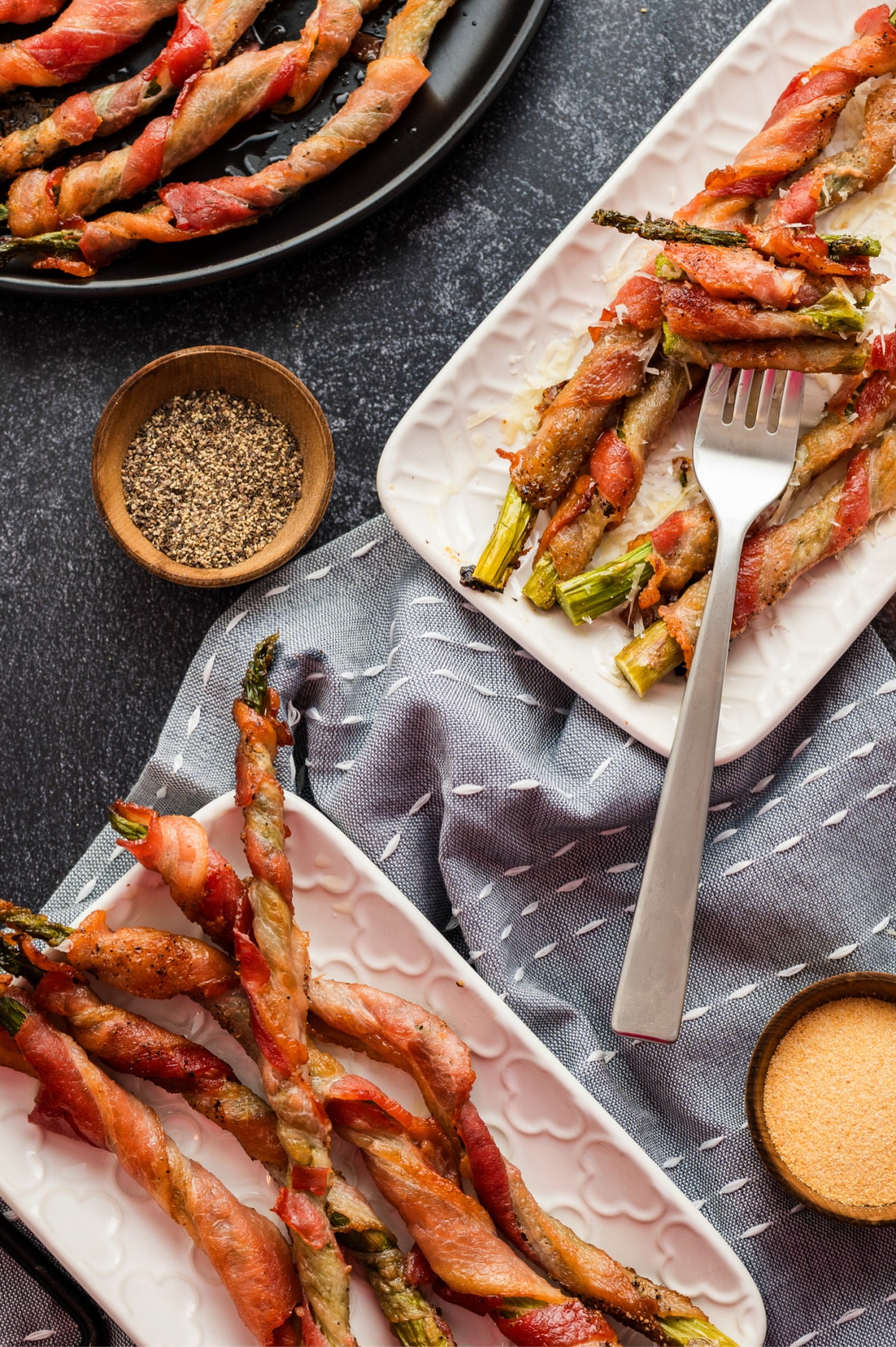 Overhead shot of two serving plates with bacon-wrapped asparagus and a fork holding a bite