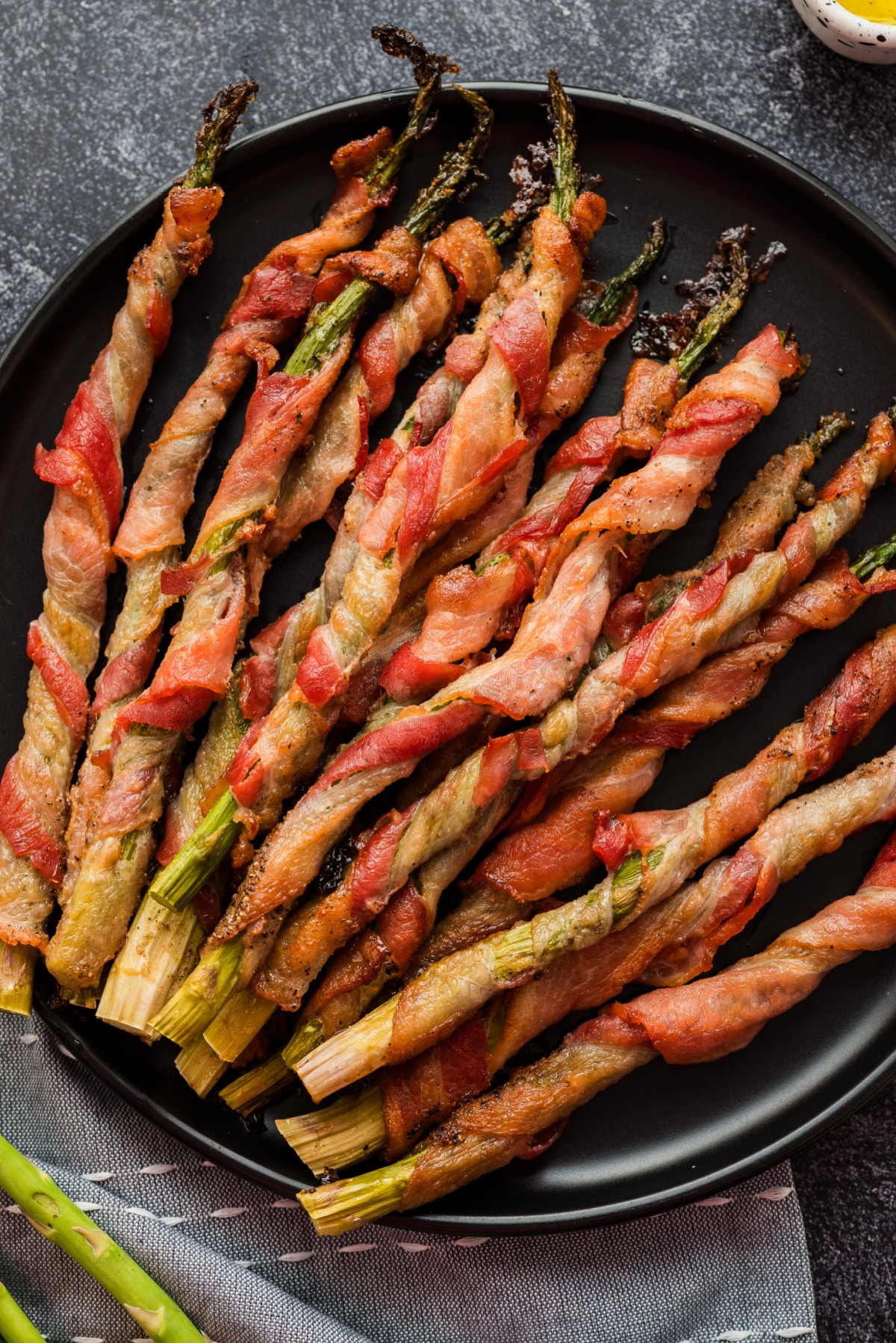 Overhead shot of roasted bacon-wrapped asparagus served on a black plate 