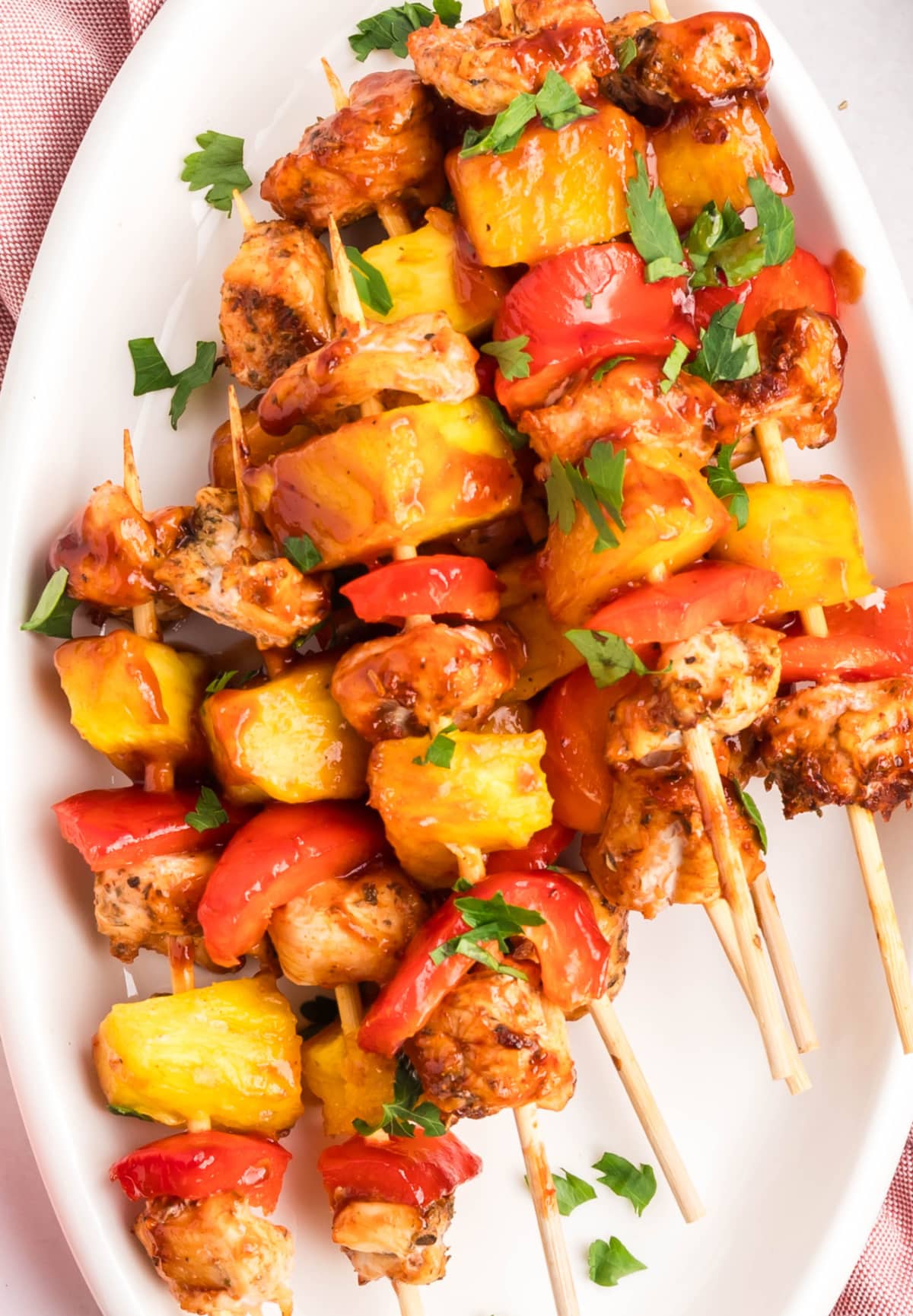 Top view of BBQ chicken skewers arranged on a white platter with caramelized pineapple