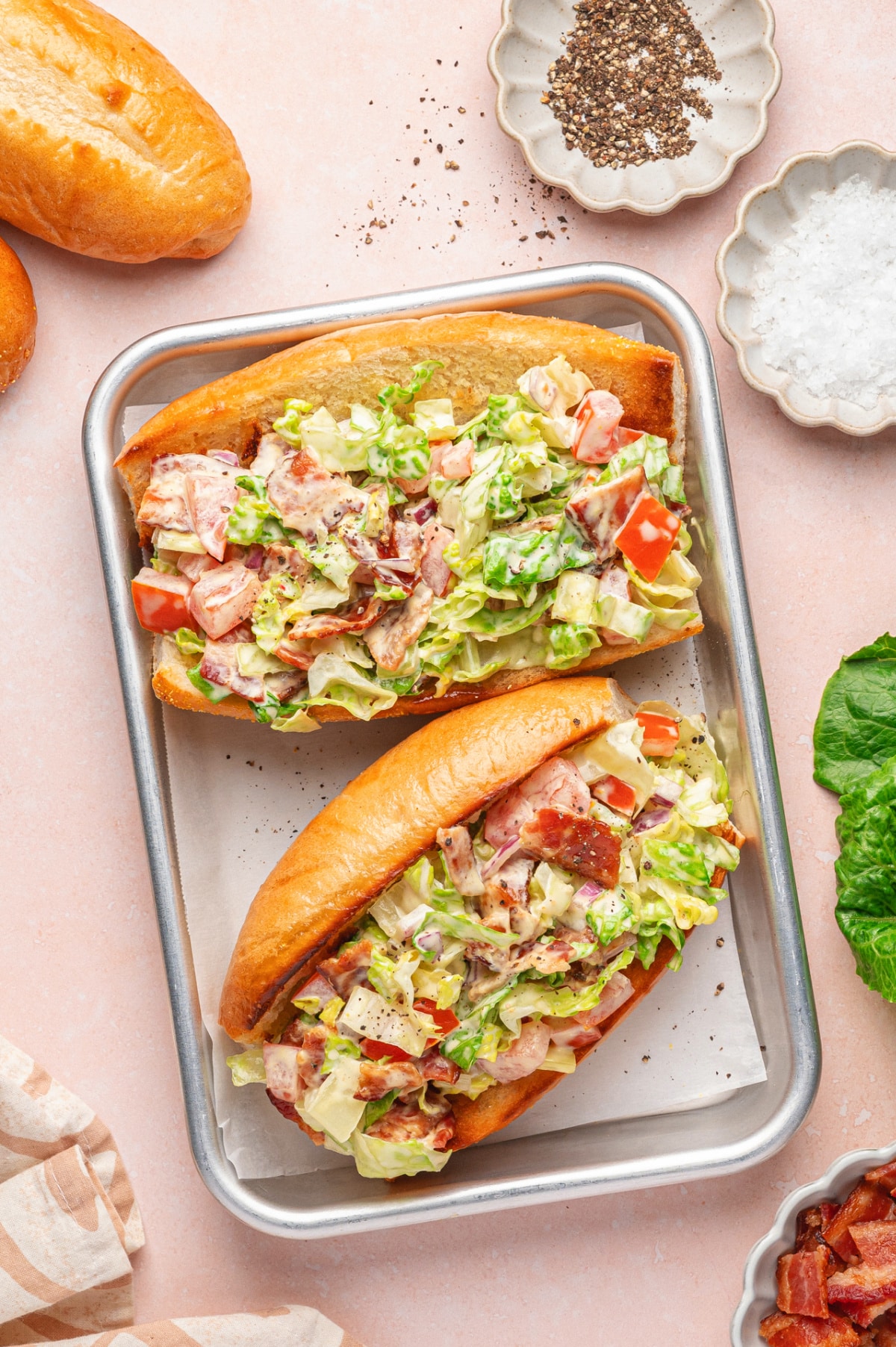 Overhead view of two freshly assembled chopped BLT hoagies on a small baking sheet with golden toasted rolls