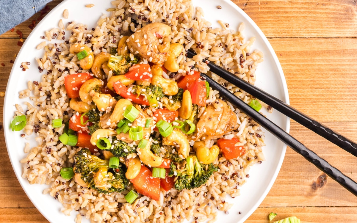 Overhead view of cashew chicken stir-fry served over white rice on a white plate