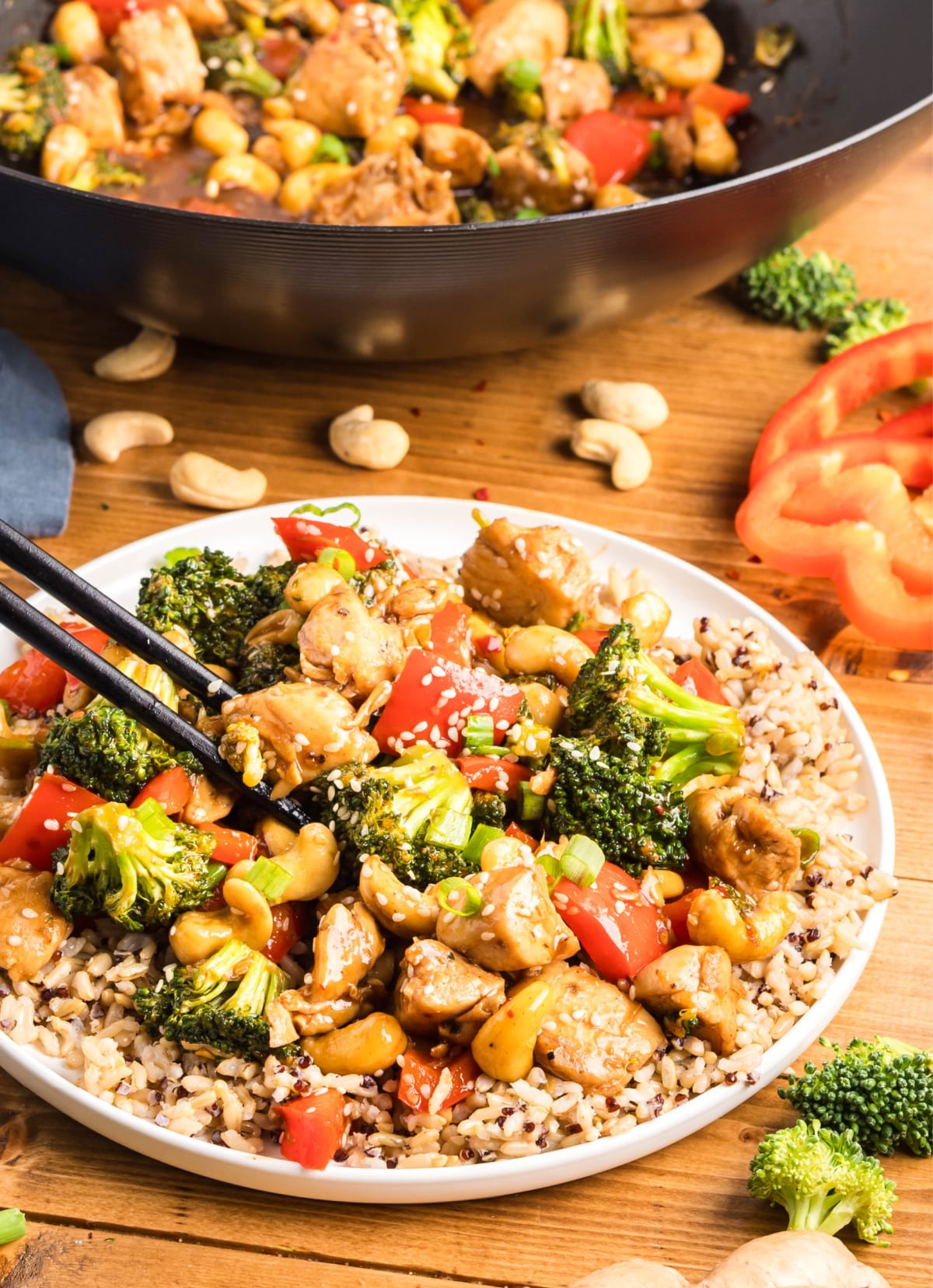Side view of chopsticks lifting a bite of cashew chicken stir-fry from a plate