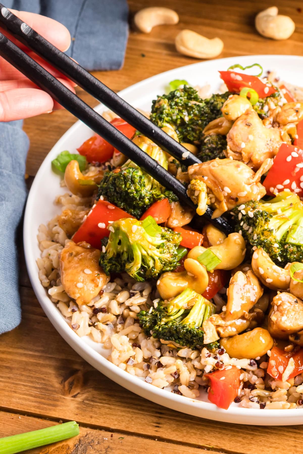 Close-up of chopsticks holding sticky cashew chicken with vegetables and cashews