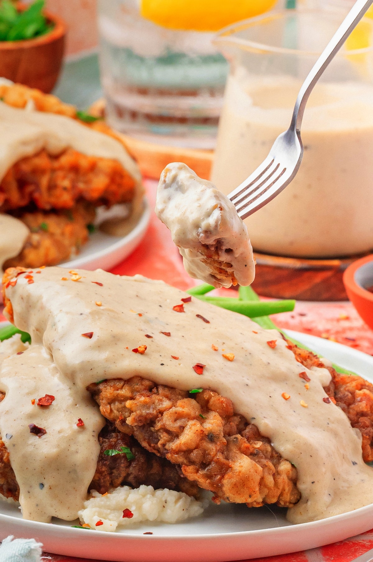 Bite of chicken fried steak on a fork held over a plate with gravy and sides