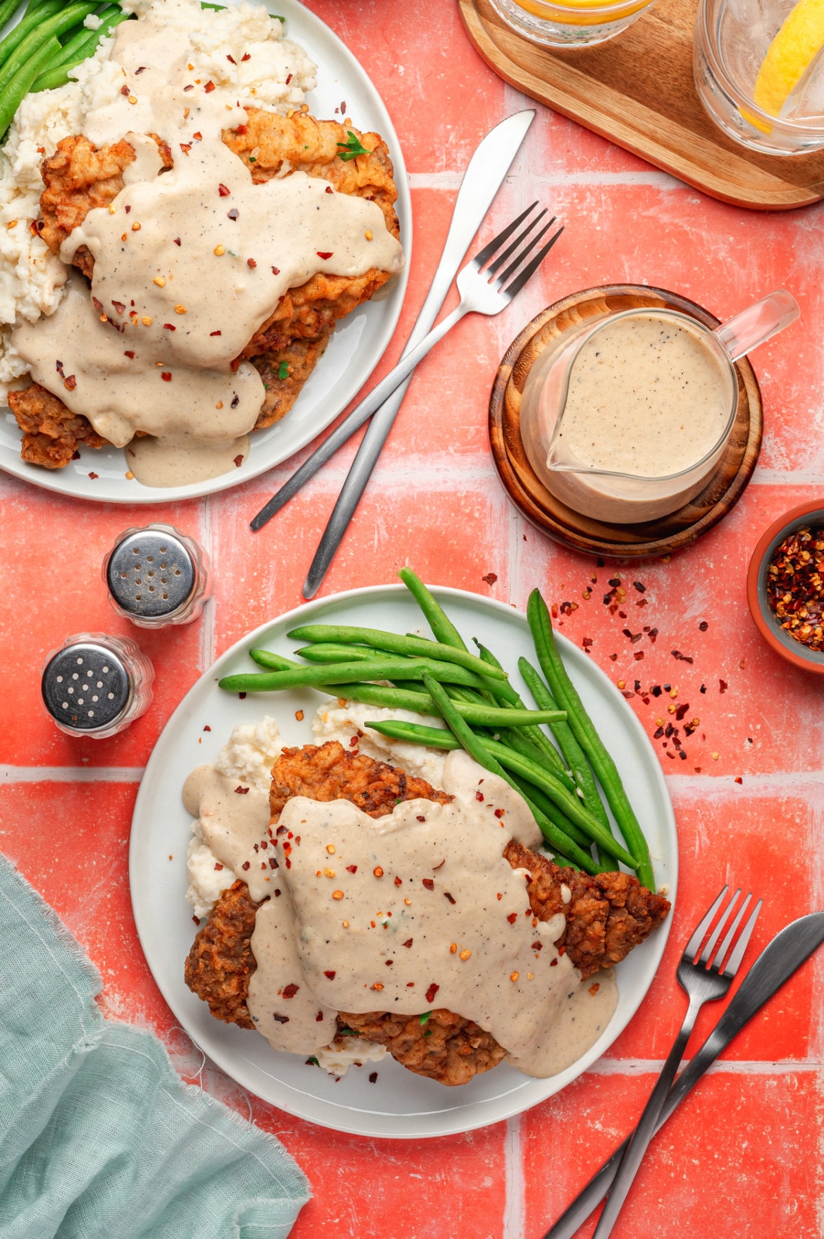 Two plates of chicken fried steak with gravy, mashed potatoes, and green beans