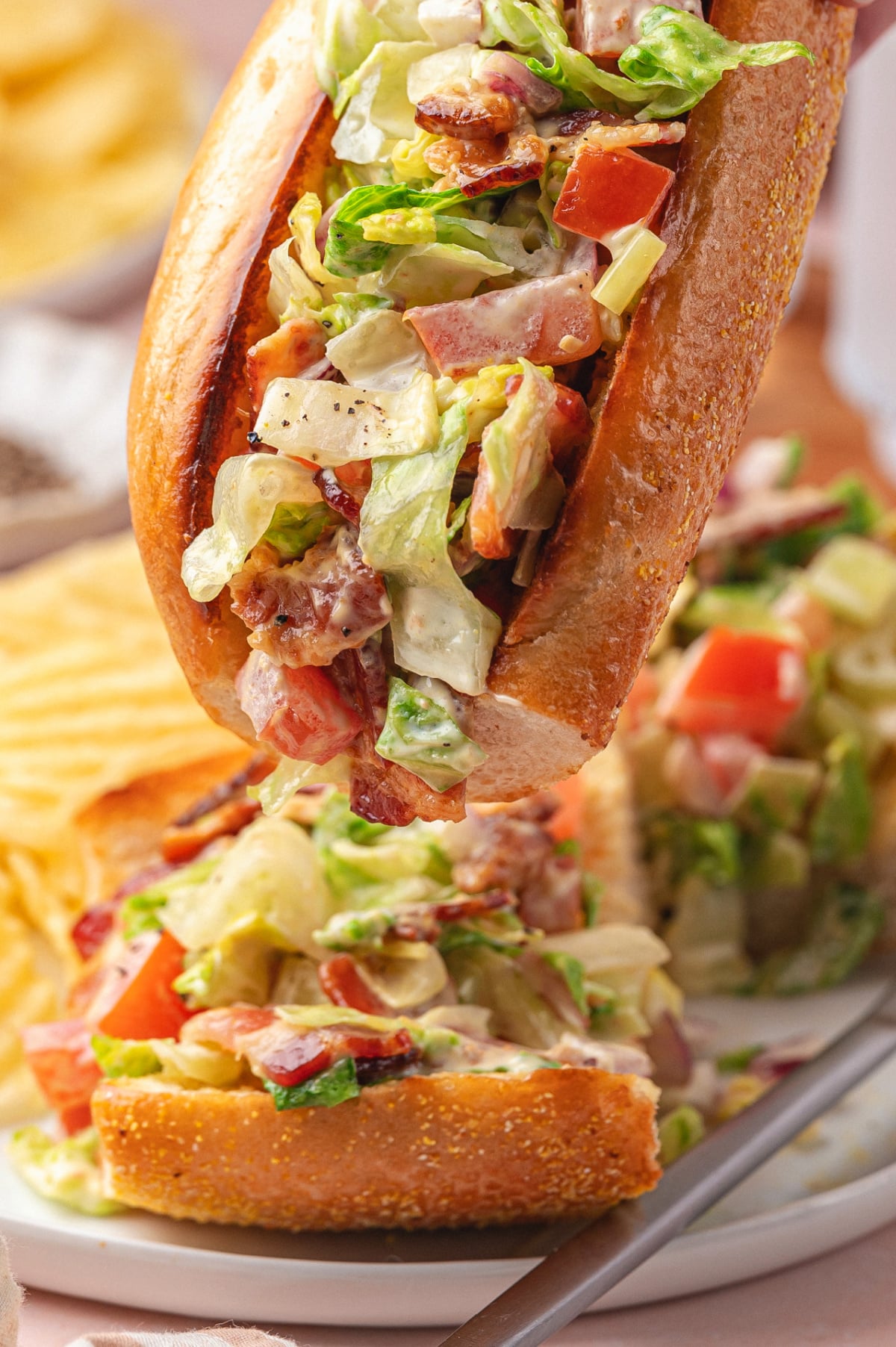 Close-up of a chopped BLT hoagie filled with creamy bacon lettuce tomato filling, with more hoagies blurred in the background.