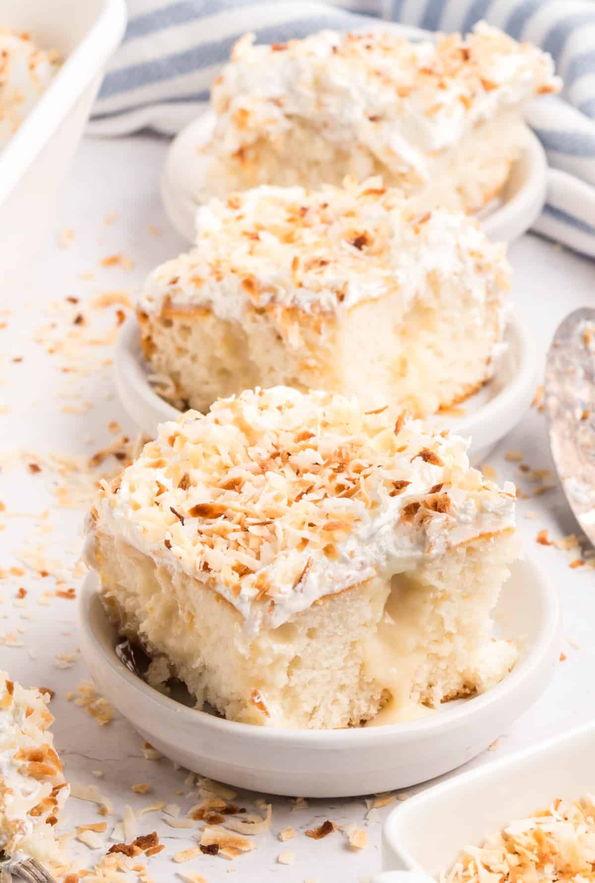 Side view of three slices of coconut poke cake showing the creamy filling and toasted coconut topping.