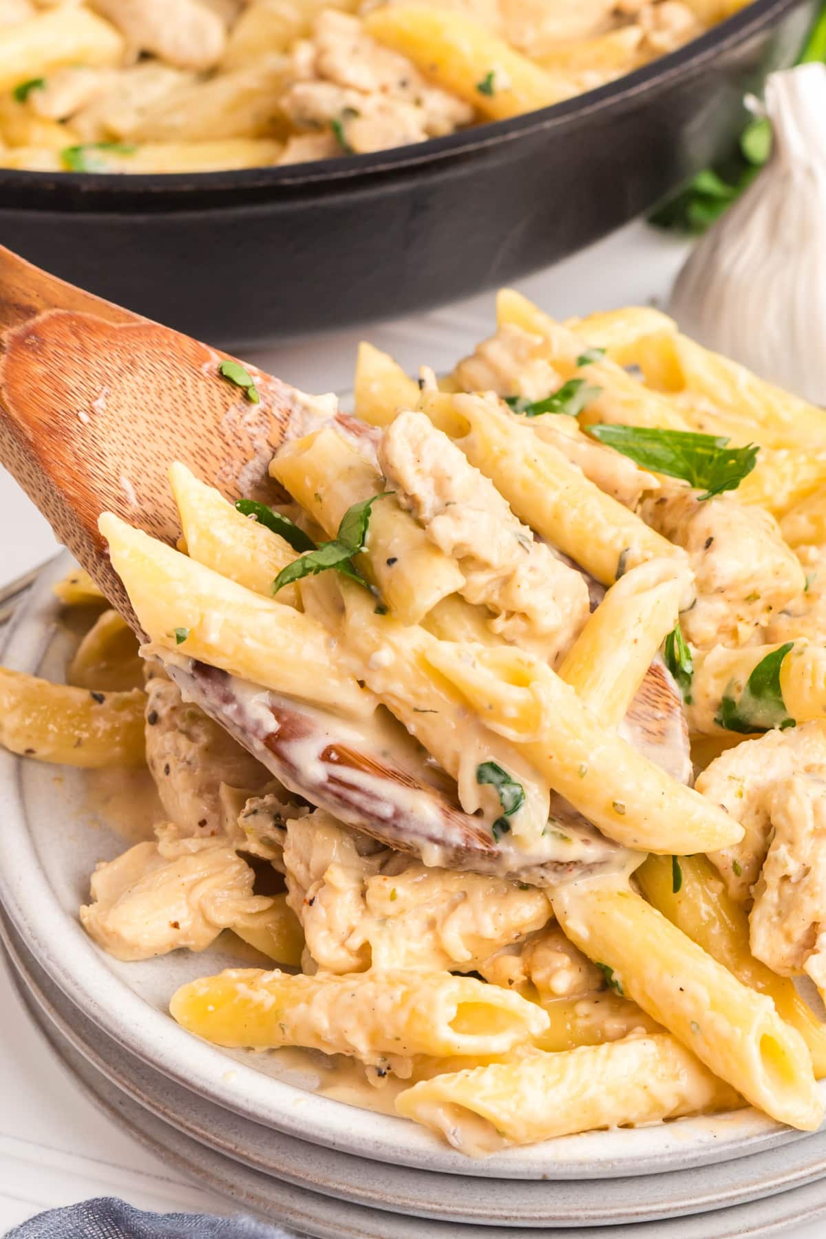 Creamy garlic chicken pasta in a skillet with a wooden spoon 