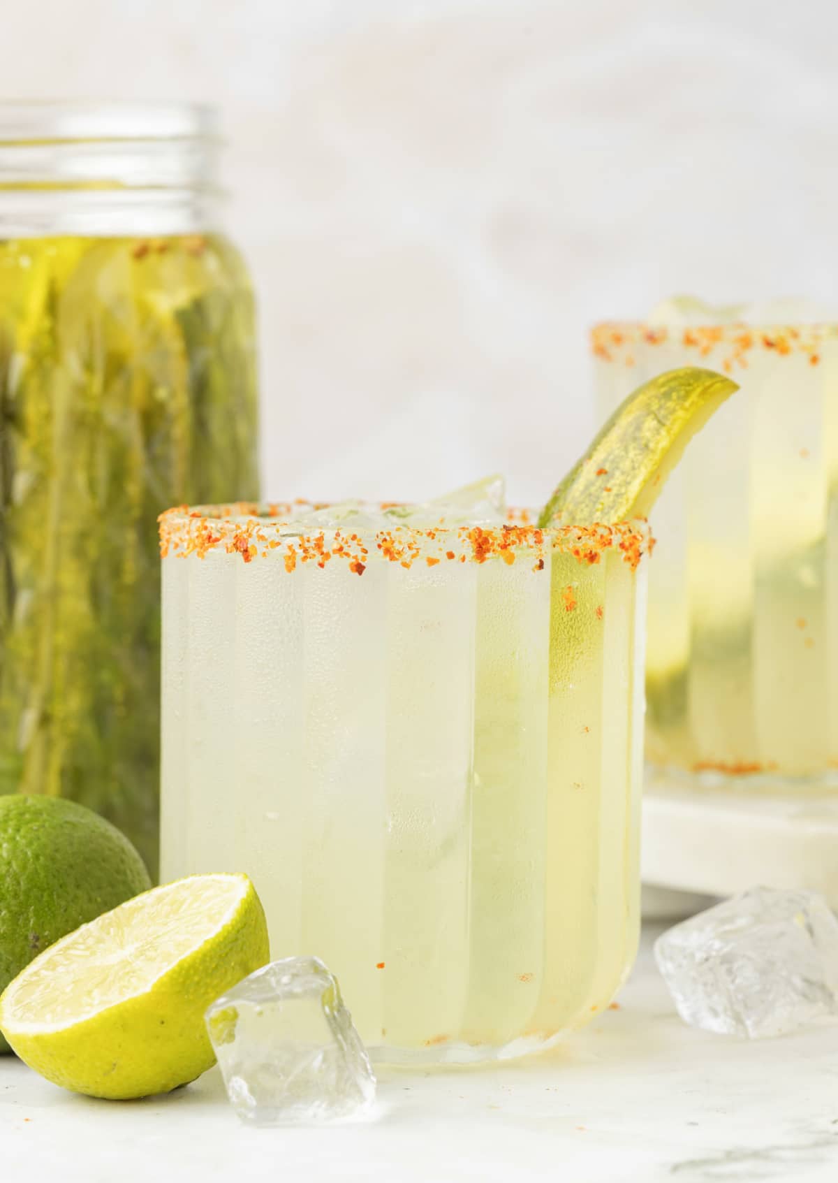 Dill Pickle Margarita with Pickles and Limes Margarita cocktail with a jar of dill pickles and fresh limes in the background