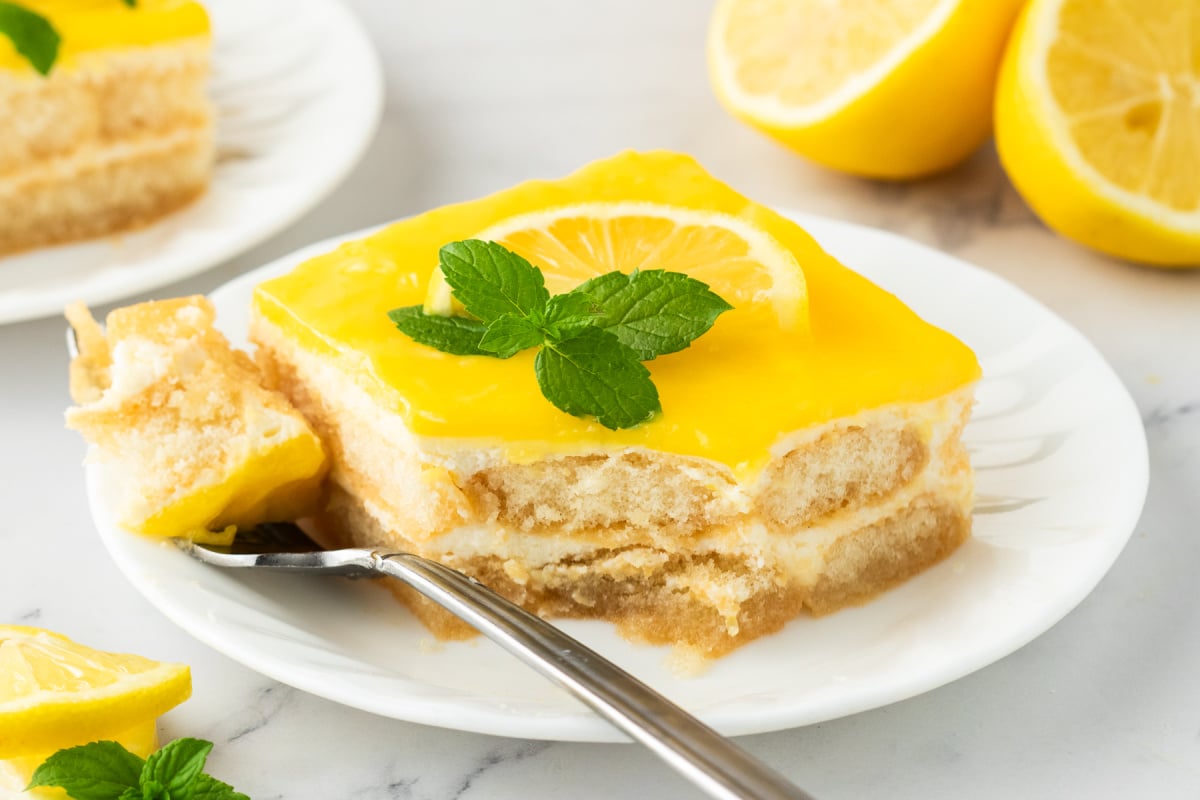 A slice of lemon tiramisu on a white plate with a bite resting on a fork.