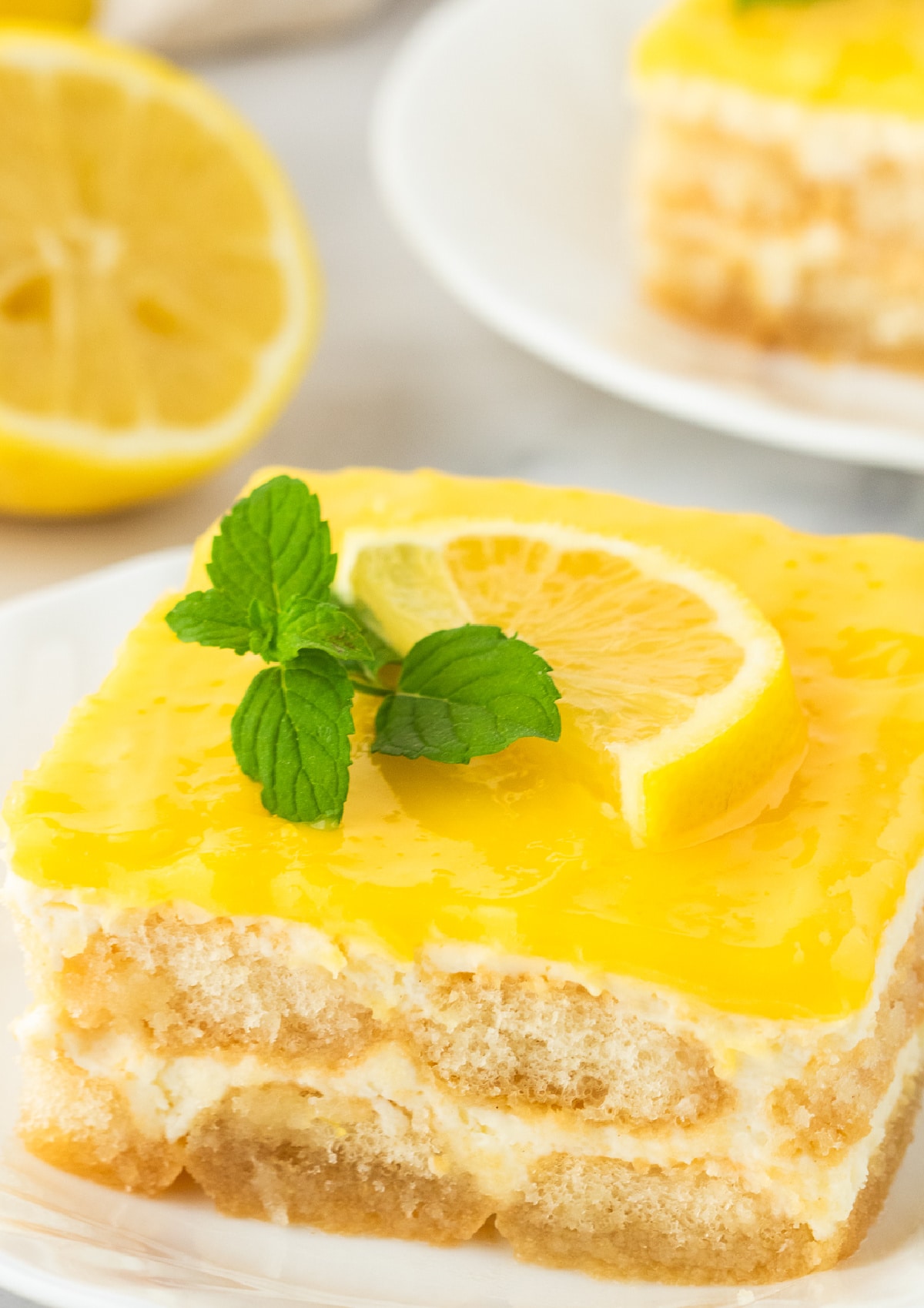 A full slice of lemon tiramisu with a sliced lemon and mint in the background.