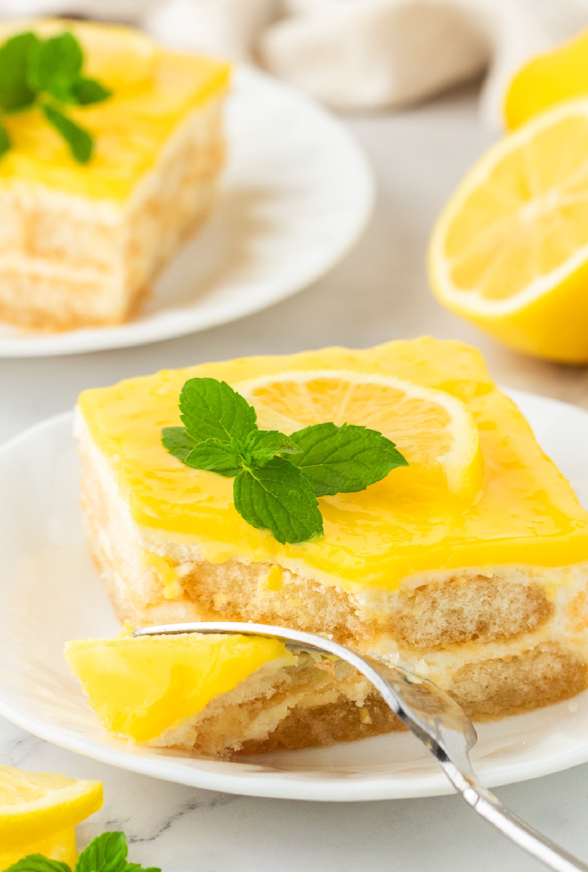 A fork pulling a bite away from a slice of lemon tiramisu.