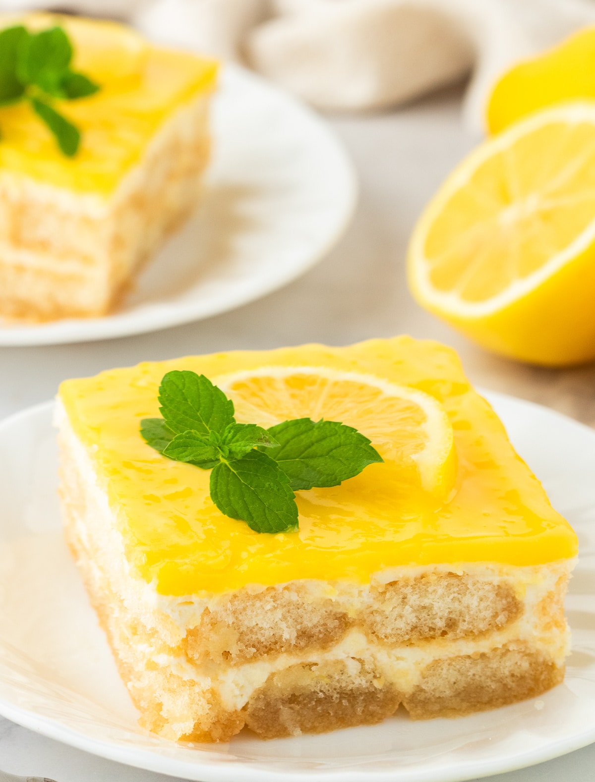 Lemon tiramisu slices on white plates, garnished with lemon slices and mint.
