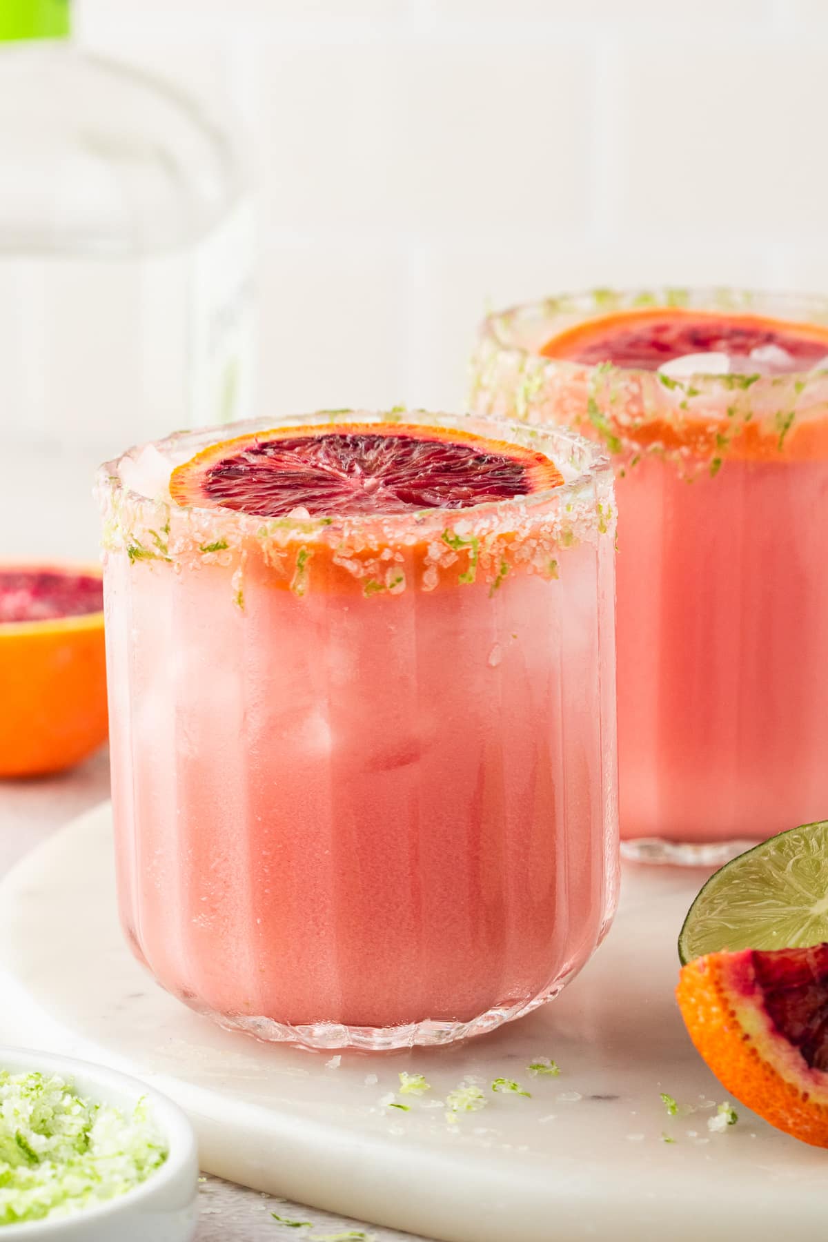 Blood Orange Coconut Margarita with Salted Lime Rim Close-up of a blood orange coconut margarita with coarse salt and lime zest rim, garnished with a blood orange wheel.