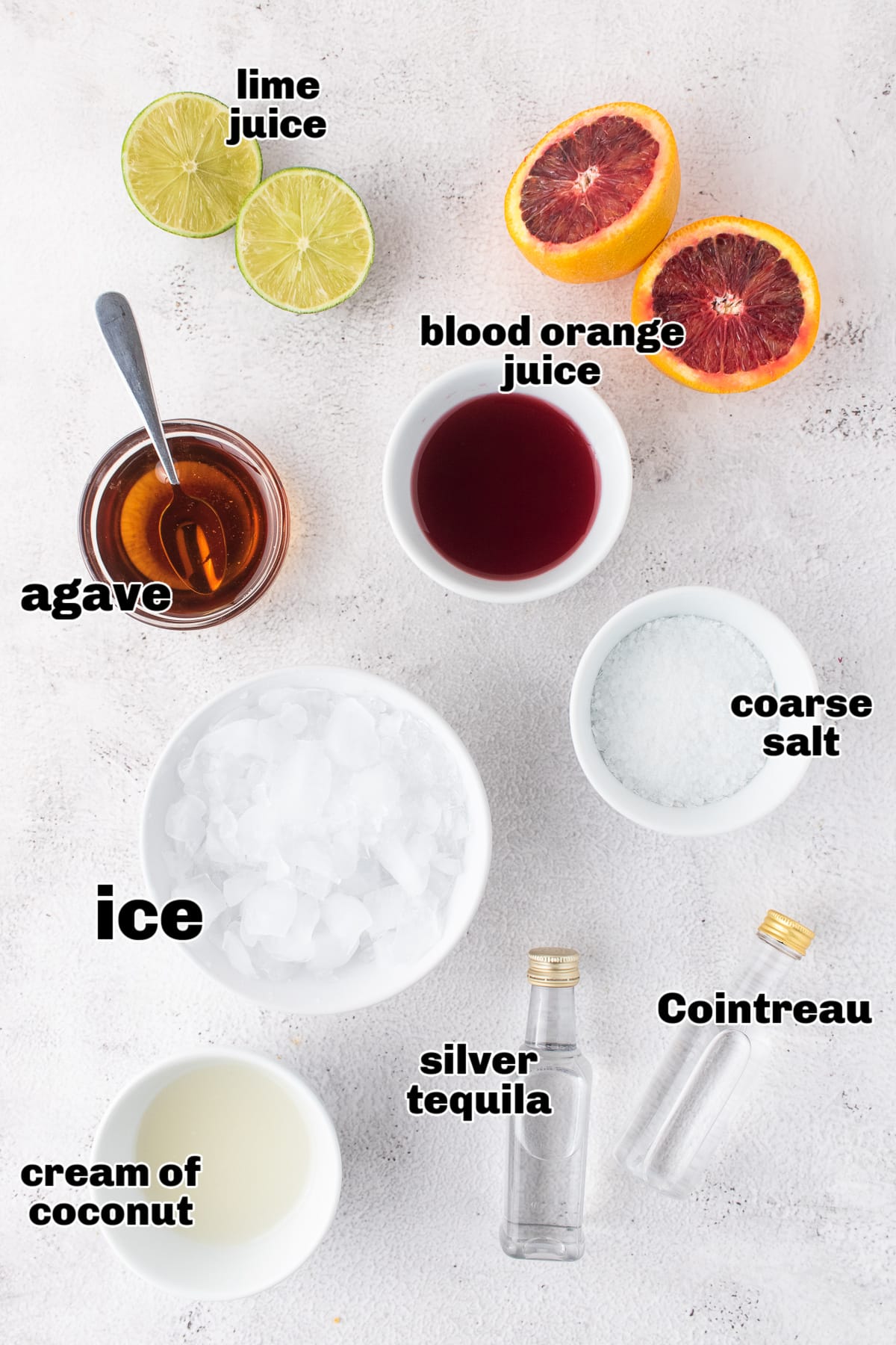 Ingredients for Blood Orange Coconut Margarita Recipe Overhead view of cocktail ingredients for a blood orange coconut margarita including lime, agave, cream of coconut, Cointreau, and silver tequila.