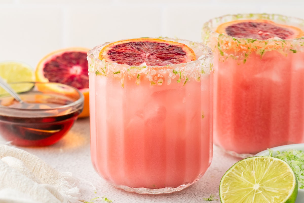 Refreshing Coconut and Blood Orange Margarita Two glasses of refreshing blood orange coconut margaritas with lime and agave in the background.
