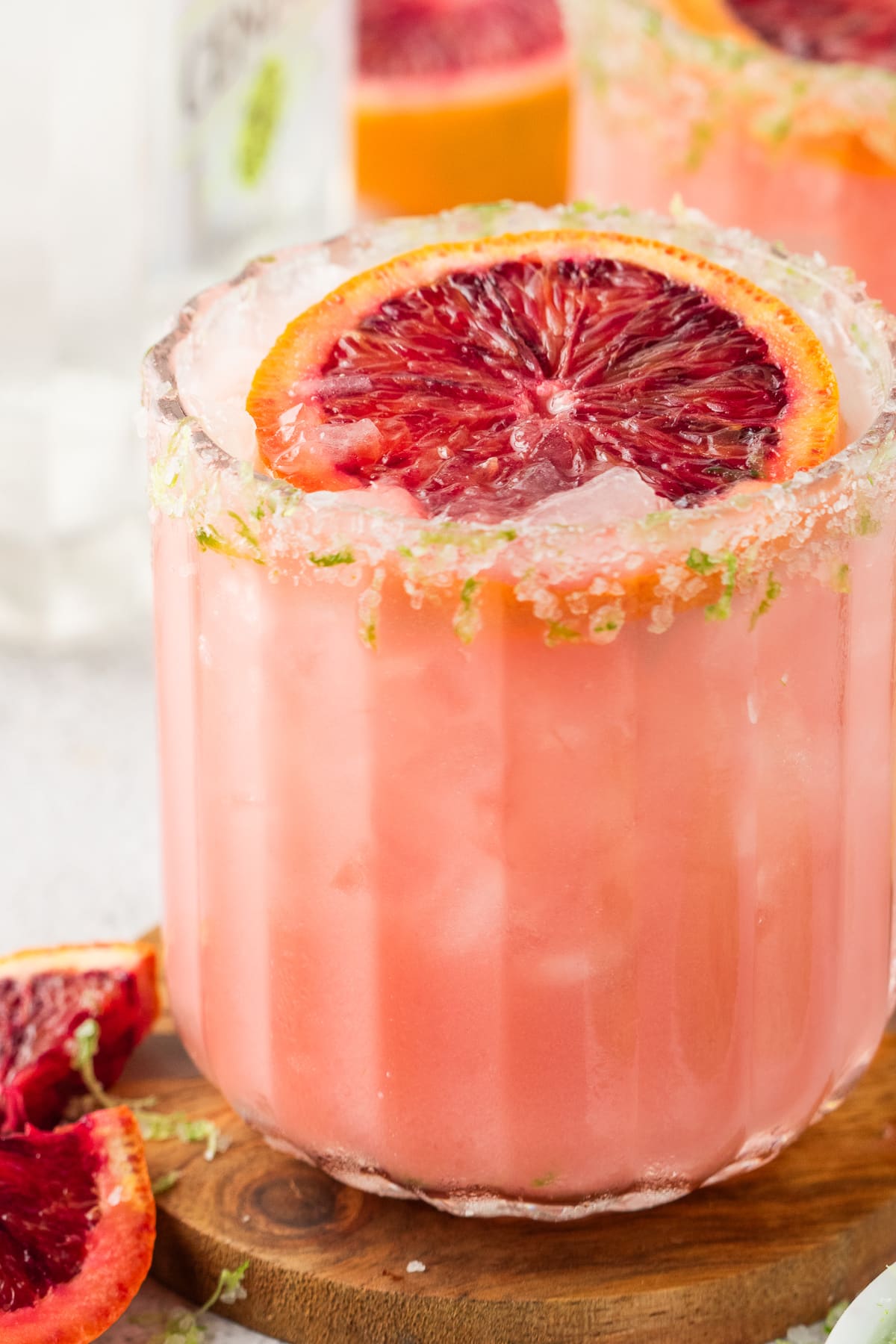 Blood Orange Coconut Margaritas Over Ice Blood orange coconut margaritas in textured glasses with visible ice, citrus zest on the rim, and a deep pink-orange color.
