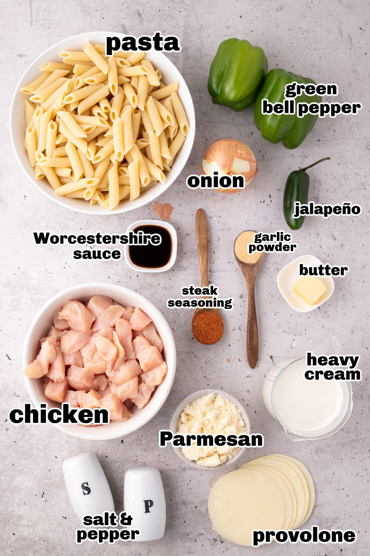 Ingredients laid out for chicken Philly cheesesteak pasta with labels Overhead view of labeled ingredients for chicken Philly cheesesteak pasta including pasta, chicken, peppers, onion, and cheeses