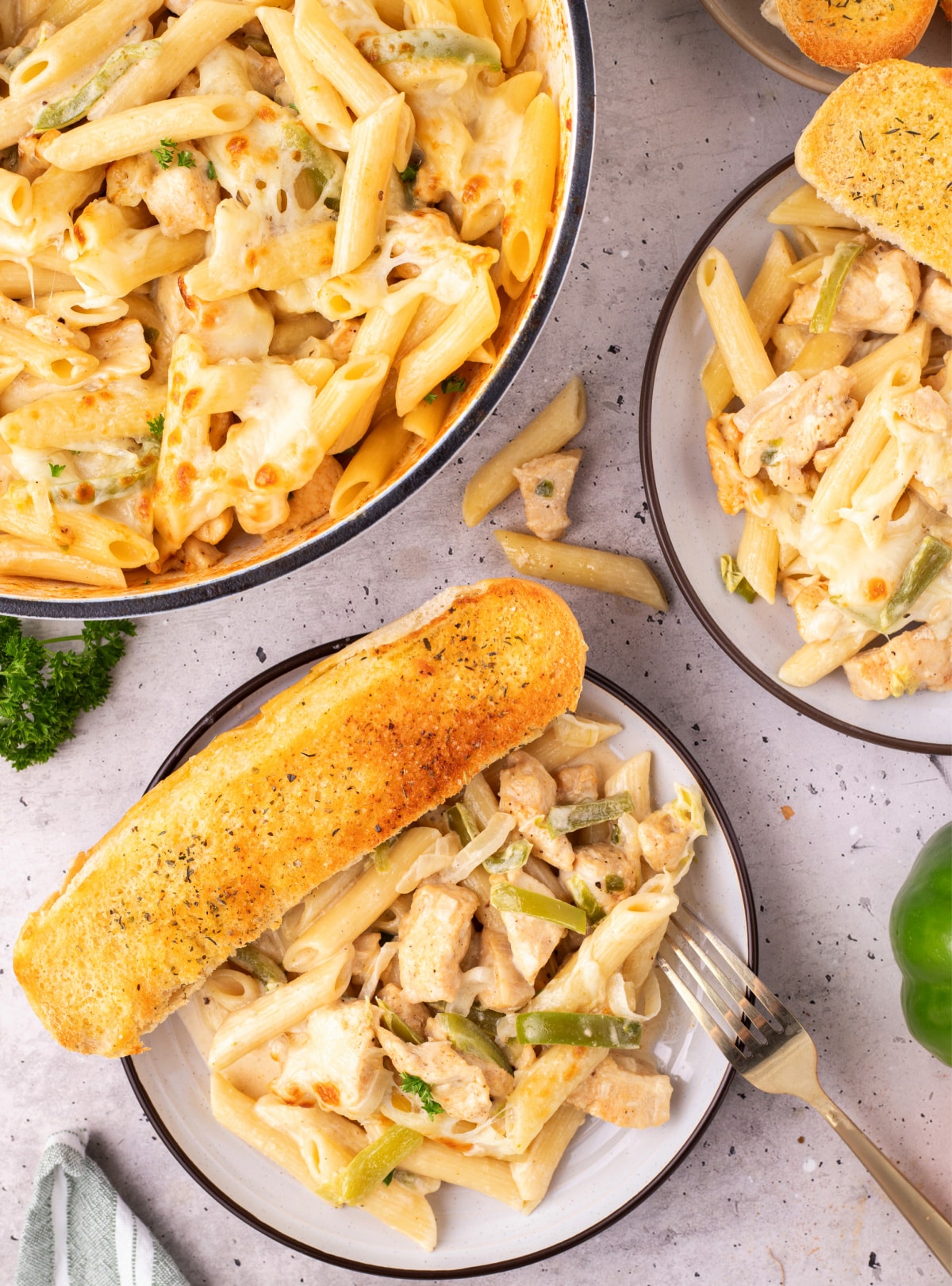 Chicken Philly cheesesteak pasta covered in provolone cheese before broiling Skillet of chicken Philly cheesesteak pasta topped with melted provolone slices